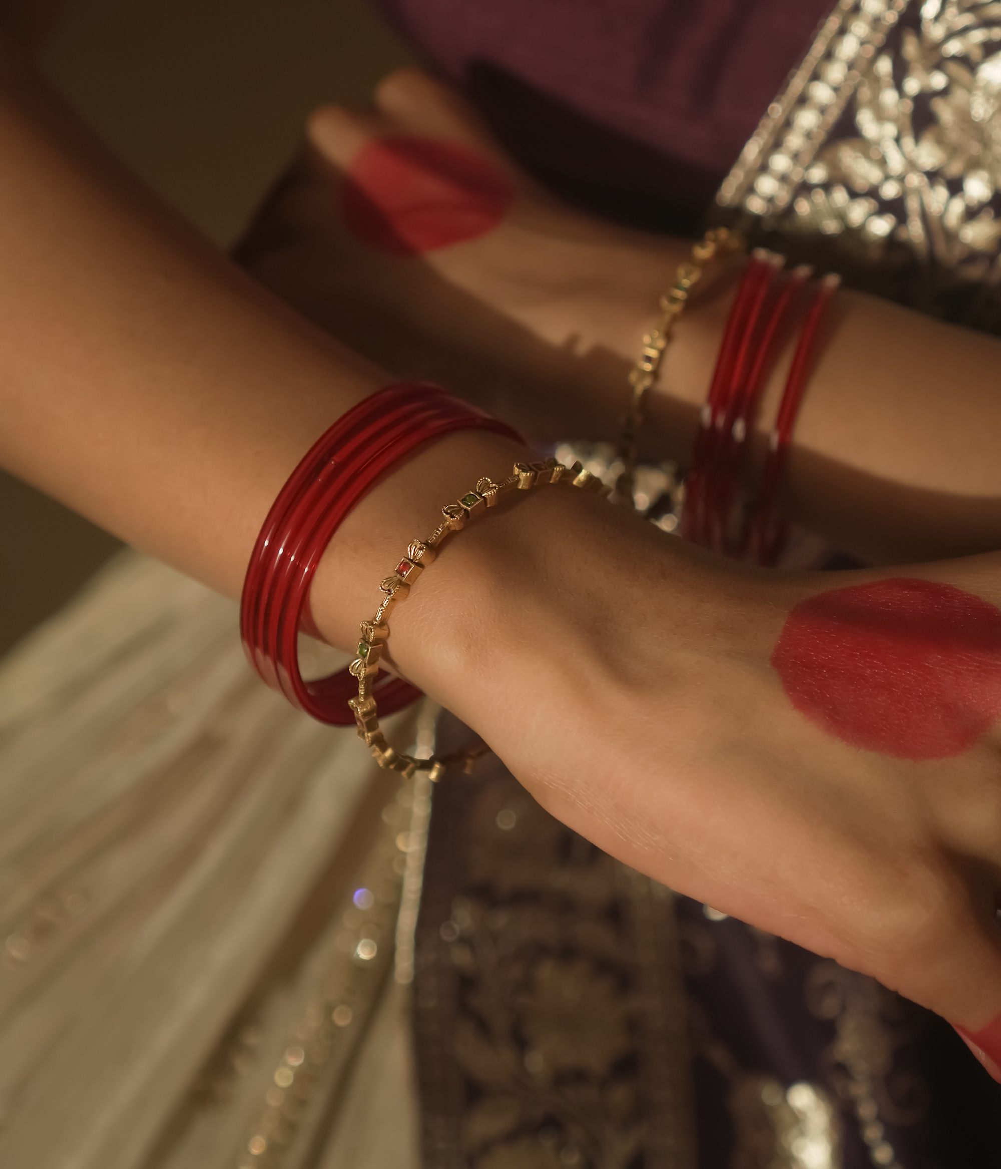 Close-up of a person's wrist wearing red bangles and a gold bracelet.