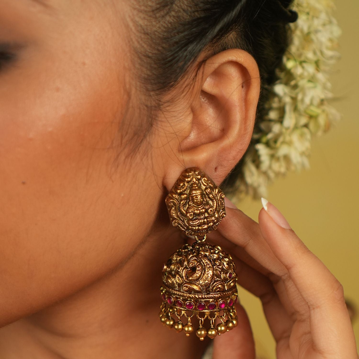 These temple-design jhumka earrings, adorned with goddess and peacock motifs, kundan stones, and golden beads, embody divine beauty and cultural heritage, offering a timeless allure that transcends eras.
