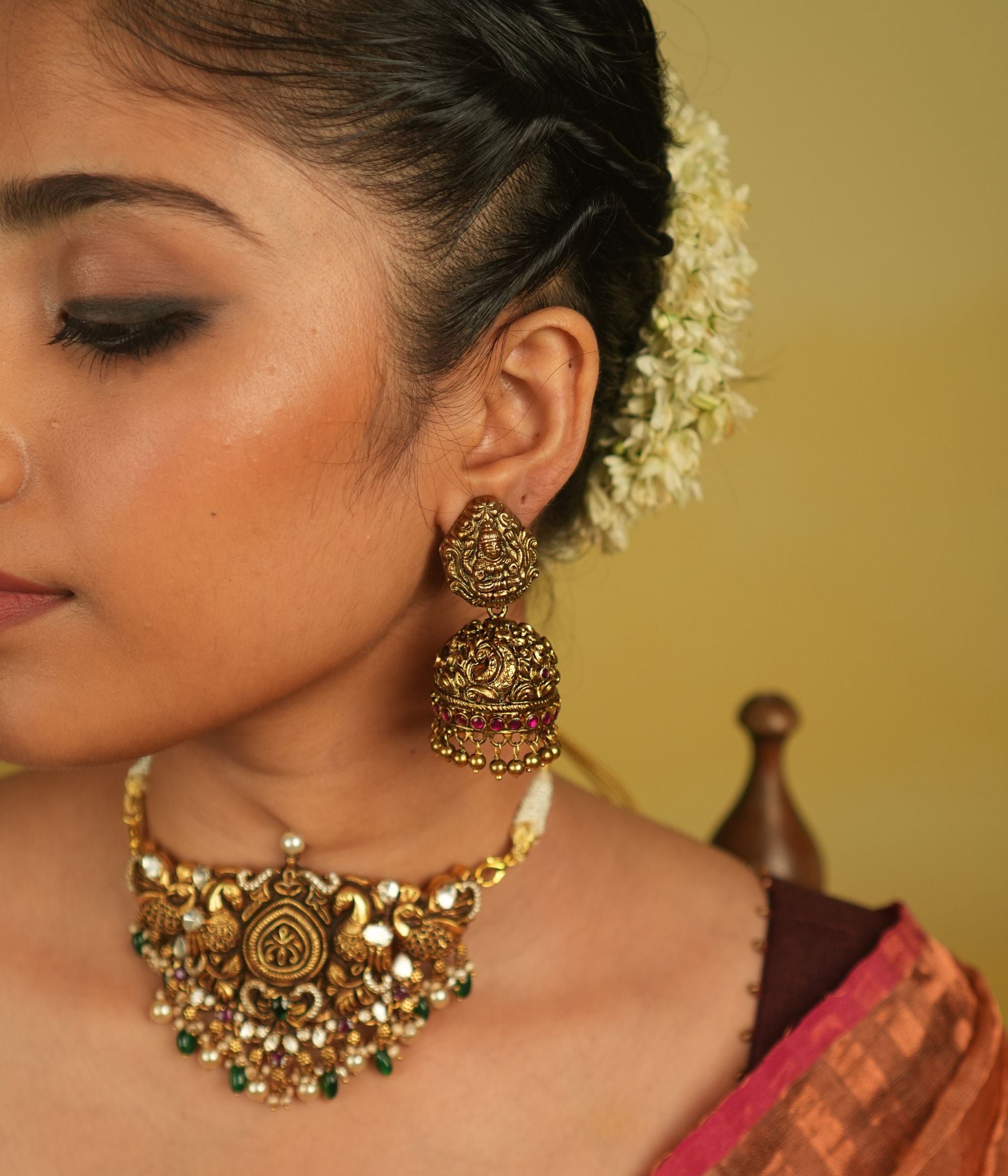 These temple-design jhumka earrings, adorned with goddess and peacock motifs, kundan stones, and golden beads, embody divine beauty and cultural heritage, offering a timeless allure that transcends eras.