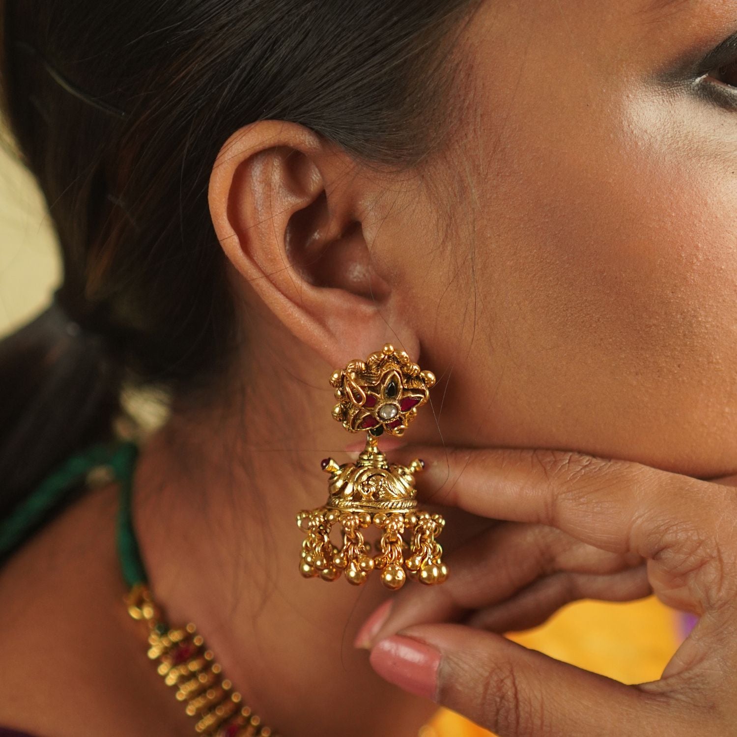 The Dora earrings combine the beauty of green and red Kundan stones, red and green spinel stones, and temple motifs, creating a fusion of contemporary elegance and rich cultural heritage.