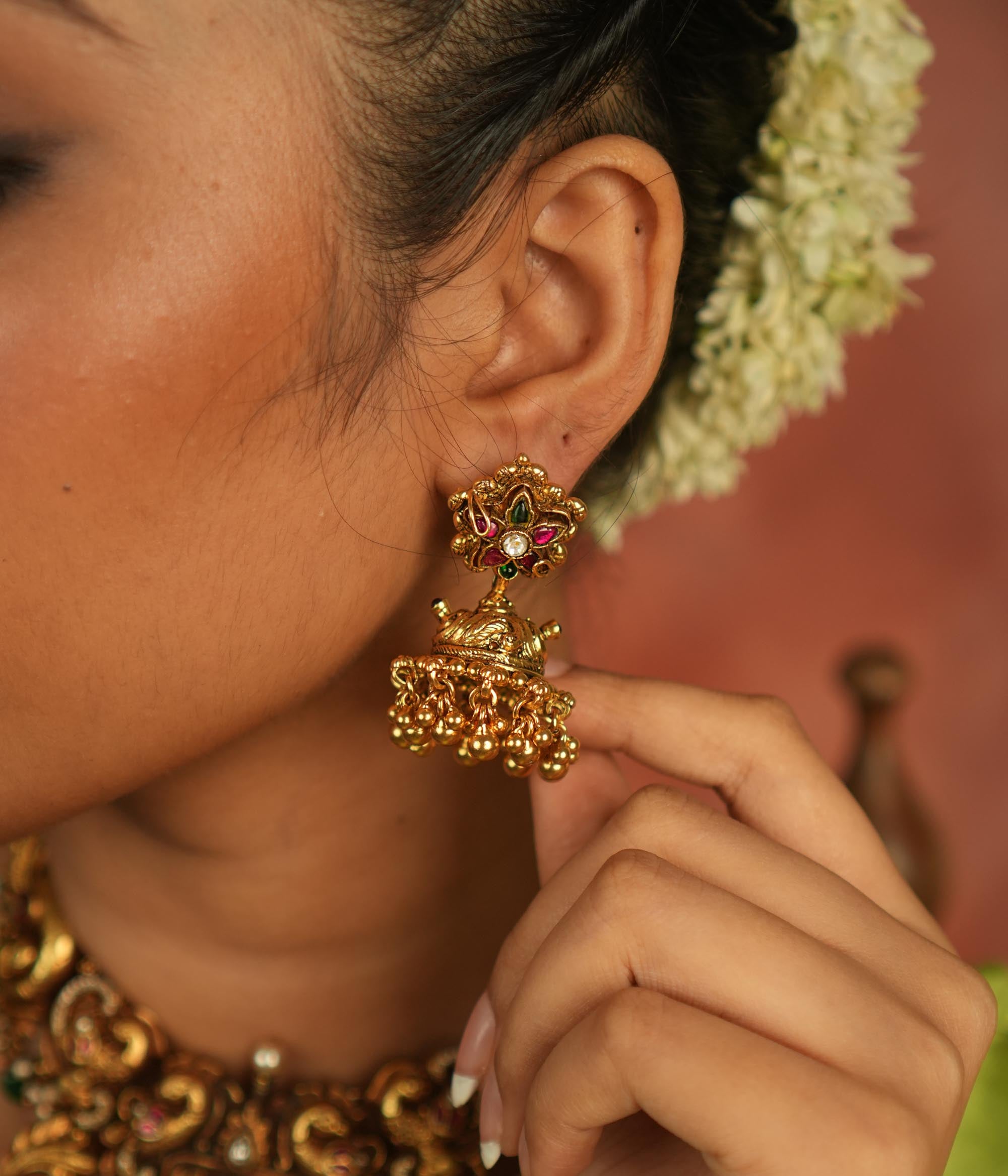 The Dora earrings combine the beauty of green and red Kundan stones, red and green spinel stones, and temple motifs, creating a fusion of contemporary elegance and rich cultural heritage.