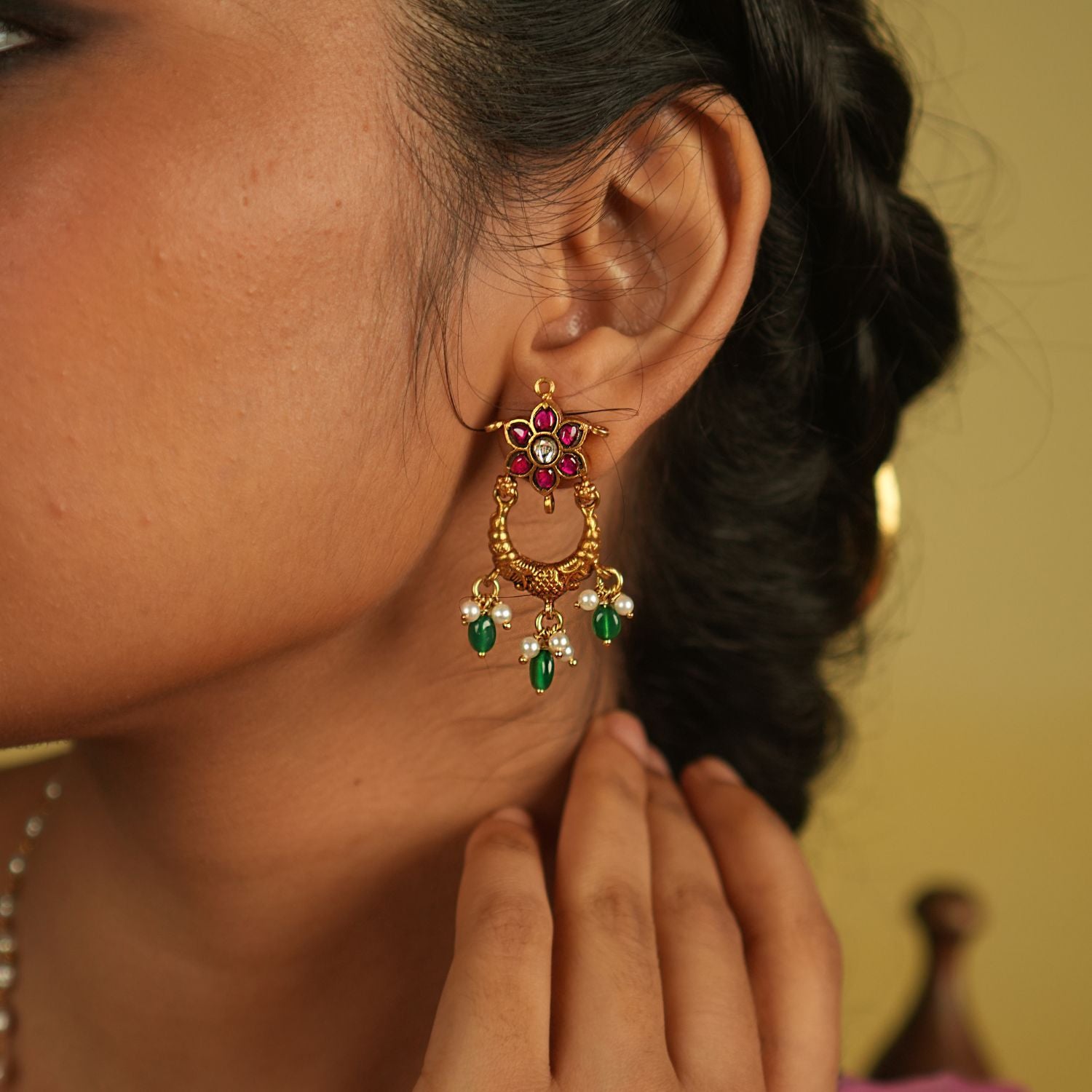 A radiant dangler earring adorned with vibrant red and green Kundan stones, where delicate petals shimmer with grace, finished with white pearl and green bead droplets for timeless allure.