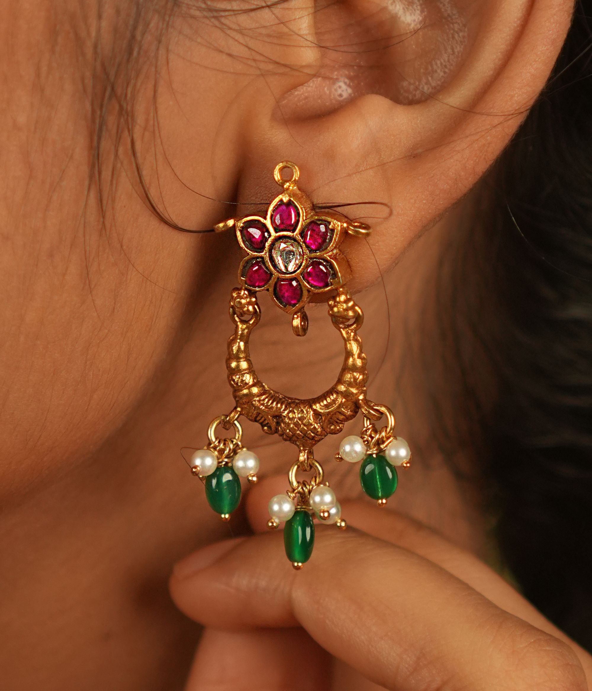 A radiant dangler earring adorned with vibrant red and green Kundan stones, where delicate petals shimmer with grace, finished with white pearl and green bead droplets for timeless allure.