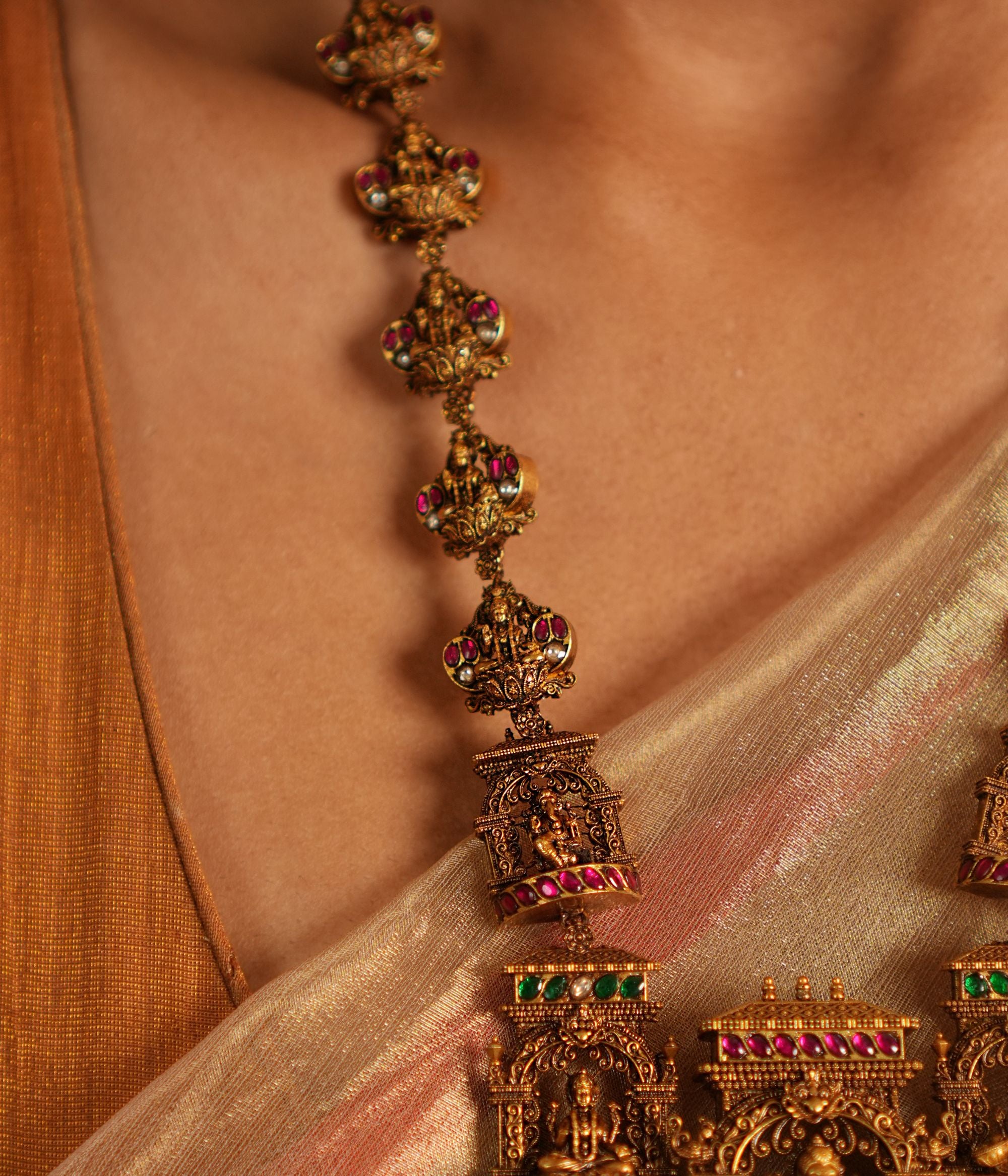 Traditional gold-plated silver temple necklace adorned with intricate carvings of deities, highlighted by Green Kundan Stones, Red Kundan Stones, pearls, and green beads. The statement centerpiece features Lord Ganesh , offering a timeless and divine elegance.