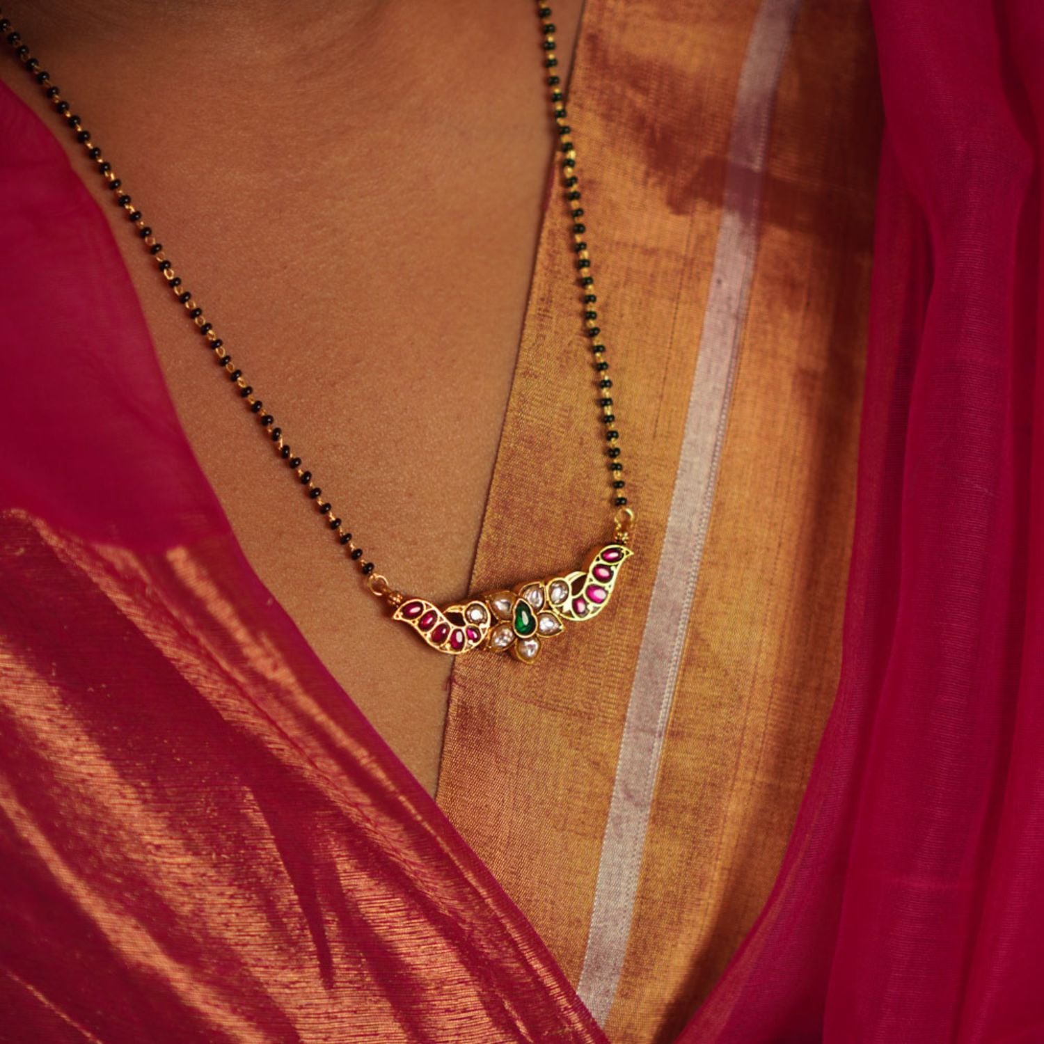 The Bithika Mangalsutra, crafted in gold-plated silver, captivates with intricate Kundan peacock motifs, reflecting the vibrancy of Indian design. Accentuated with red, white, and green Kundan stones and delicate freshwater pearls, it embodies timeless elegance.