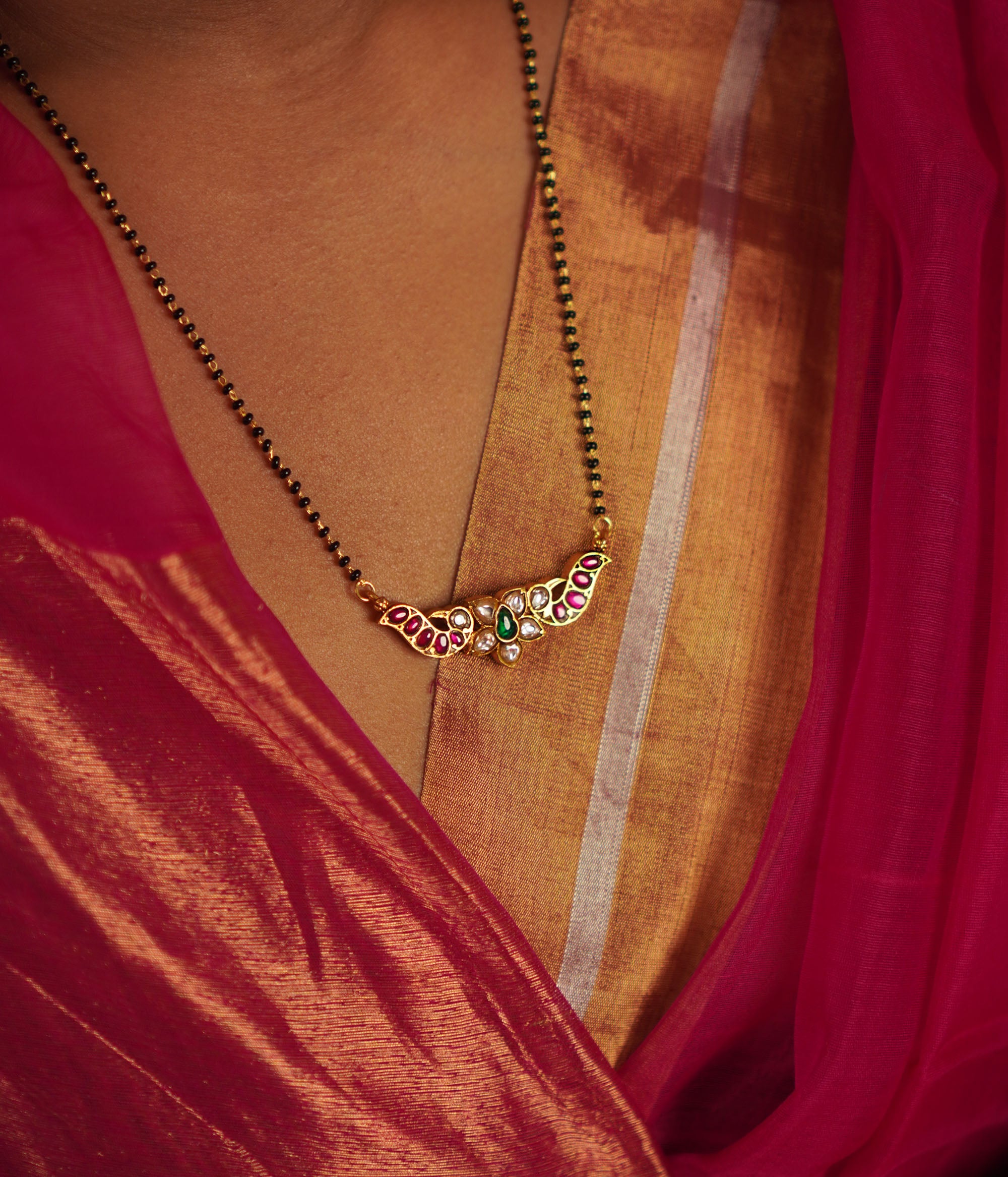 The Bithika Mangalsutra, crafted in gold-plated silver, captivates with intricate Kundan peacock motifs, reflecting the vibrancy of Indian design. Accentuated with red, white, and green Kundan stones and delicate freshwater pearls, it embodies timeless elegance.