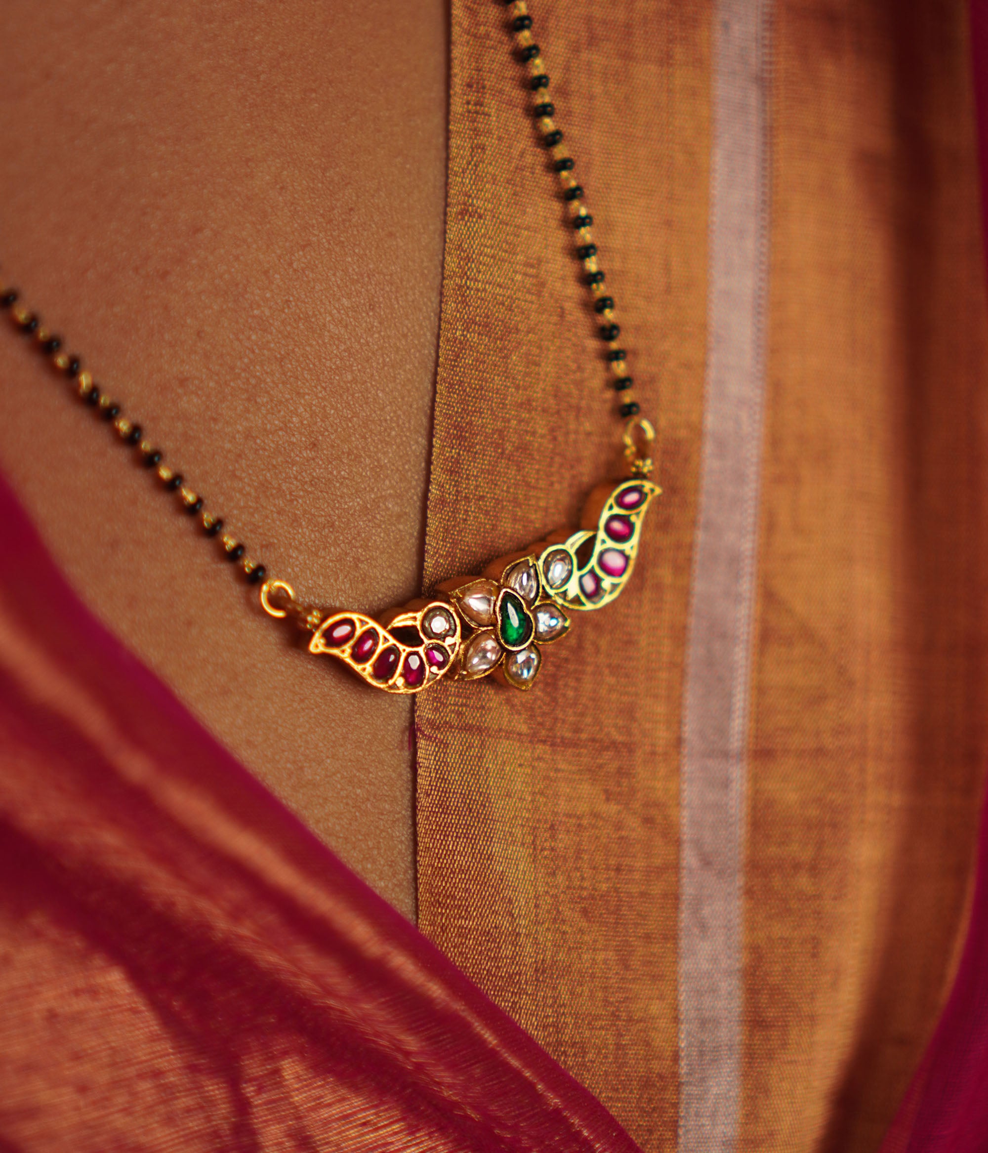 The Bithika Mangalsutra, crafted in gold-plated silver, captivates with intricate Kundan peacock motifs, reflecting the vibrancy of Indian design. Accentuated with red, white, and green Kundan stones and delicate freshwater pearls, it embodies timeless elegance.