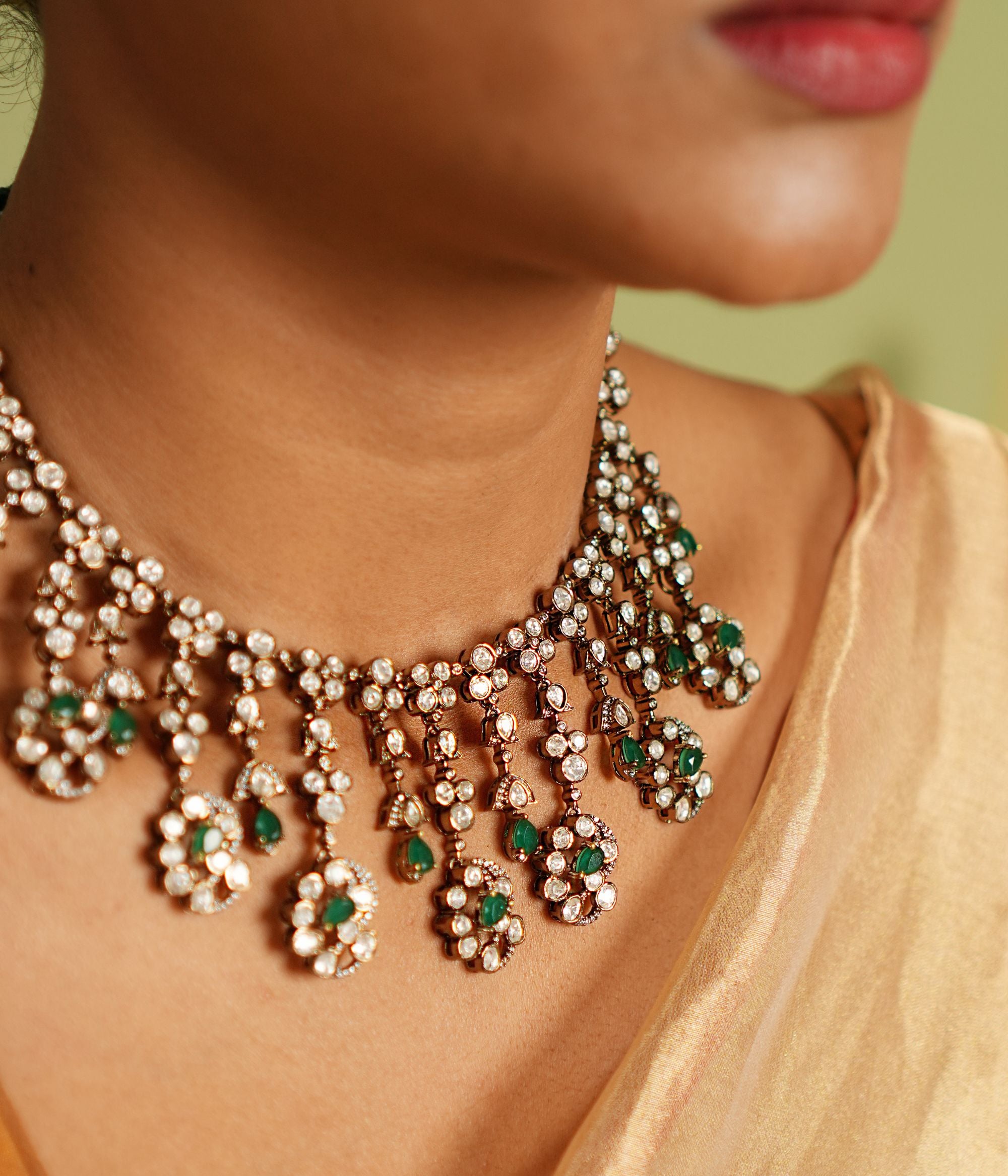Echoes of a bygone era reborn! This gold-plated silver necklace features floral-shaped droplets adorned with Polki, CZ stones, and green spinal gems, cascading like delicate vines. A timeless blend of Victorian charm and graceful allure.