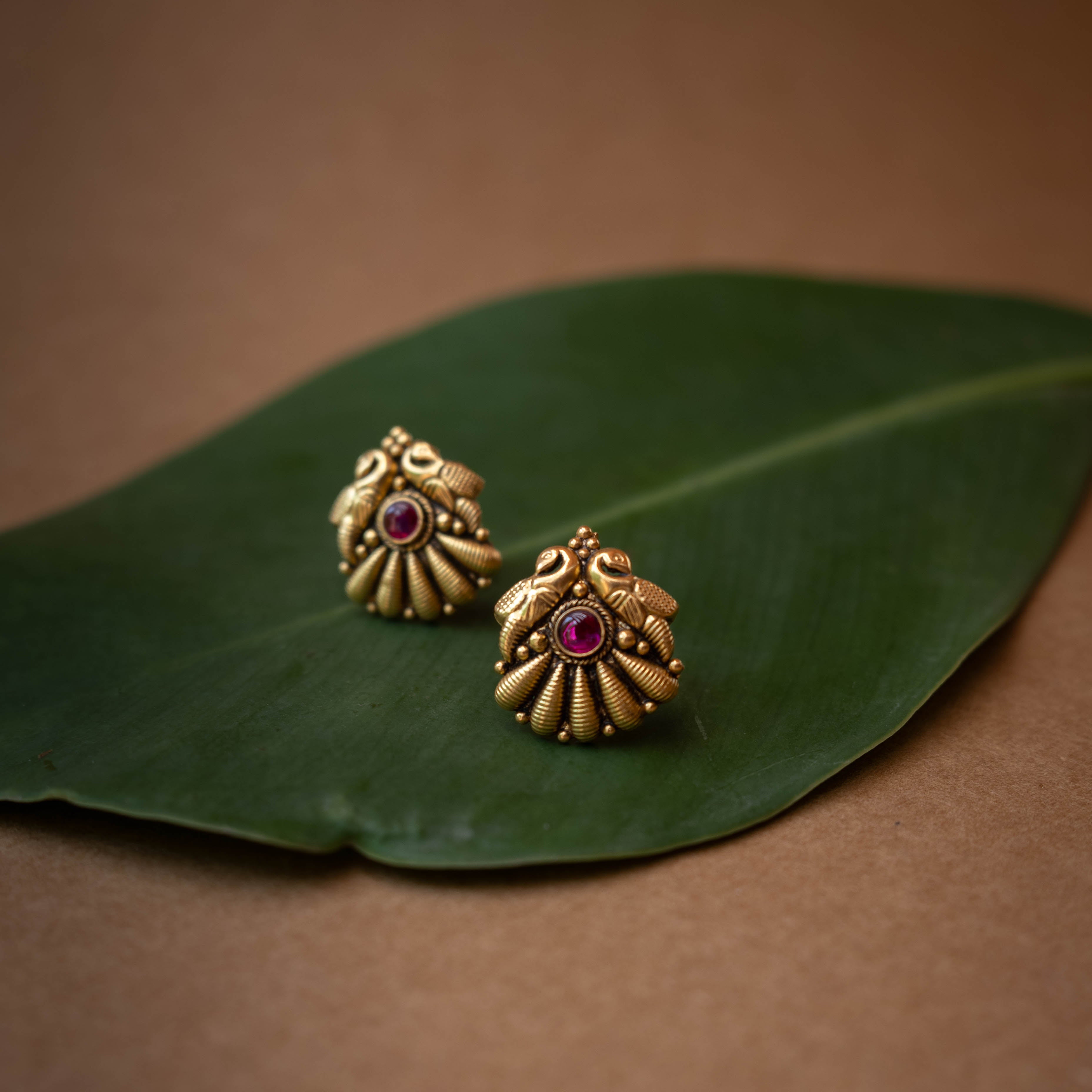 Traditional stud earrings with a central red stone and a stylized peacock and fan design.