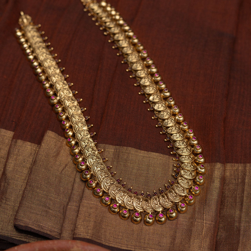Long Kasu Mala necklace featuring an array of antique-finished gold (likely 92.5 sterling silver) coins depicting Goddess Lakshmi, delicately accented with ruby-toned stones, a timeless symbol of blessings and cultural richness.