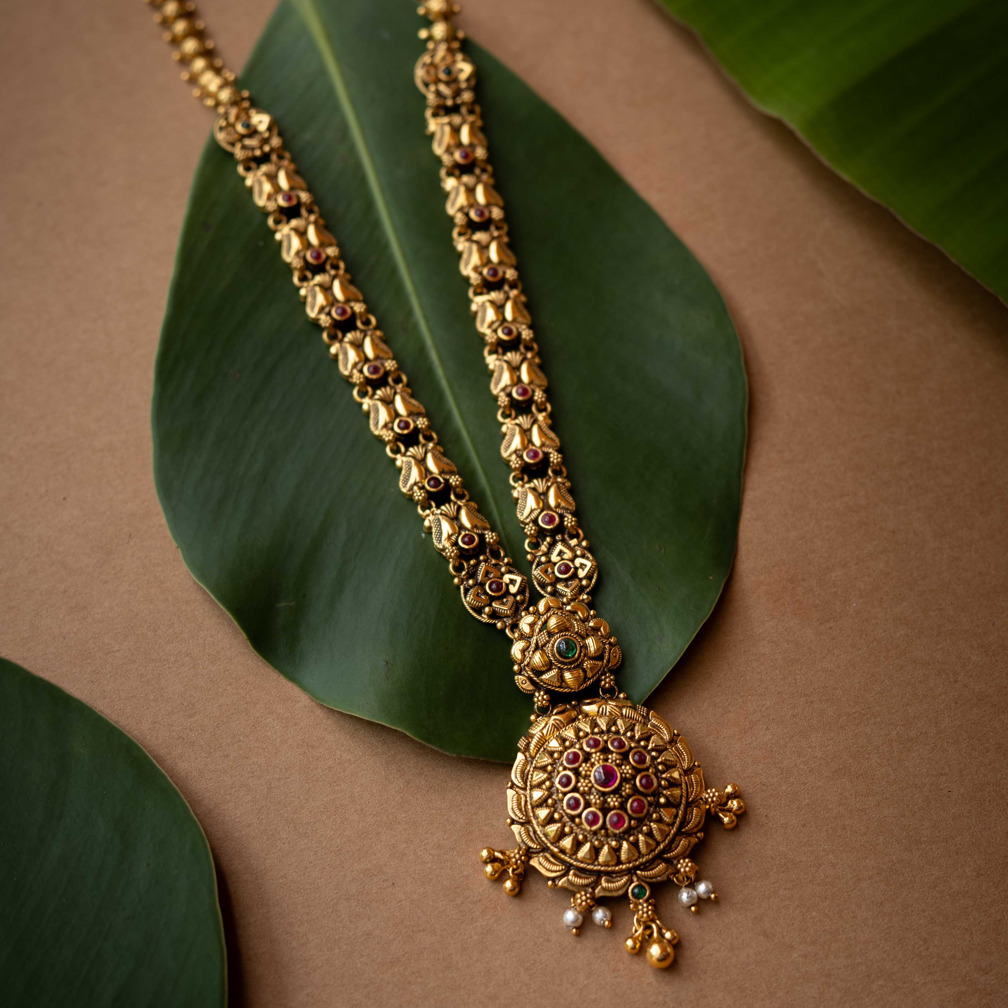 Antique gold temple necklace with lotus motifs and ruby-green stone accents from Temple Collection.