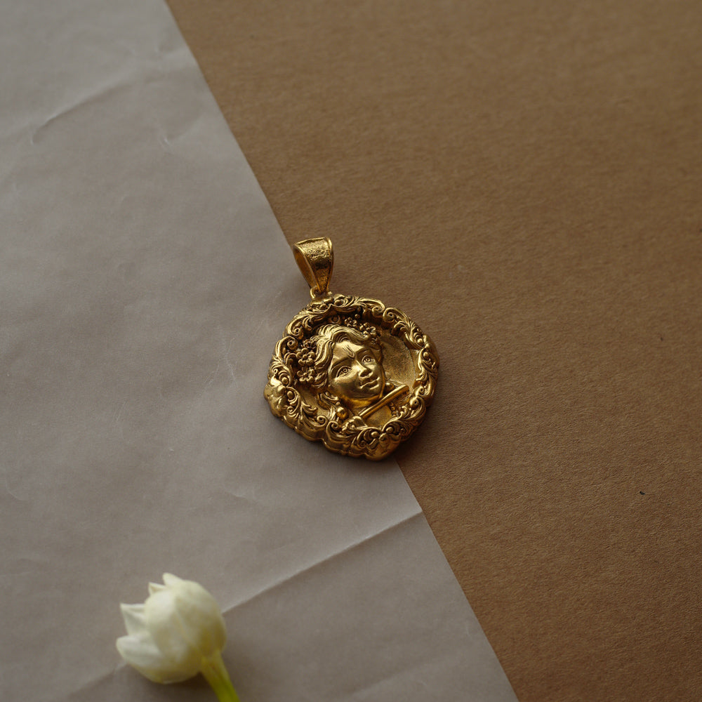Round gold pendant with a central relief of a child's face. The face is surrounded by a detailed filigree border.