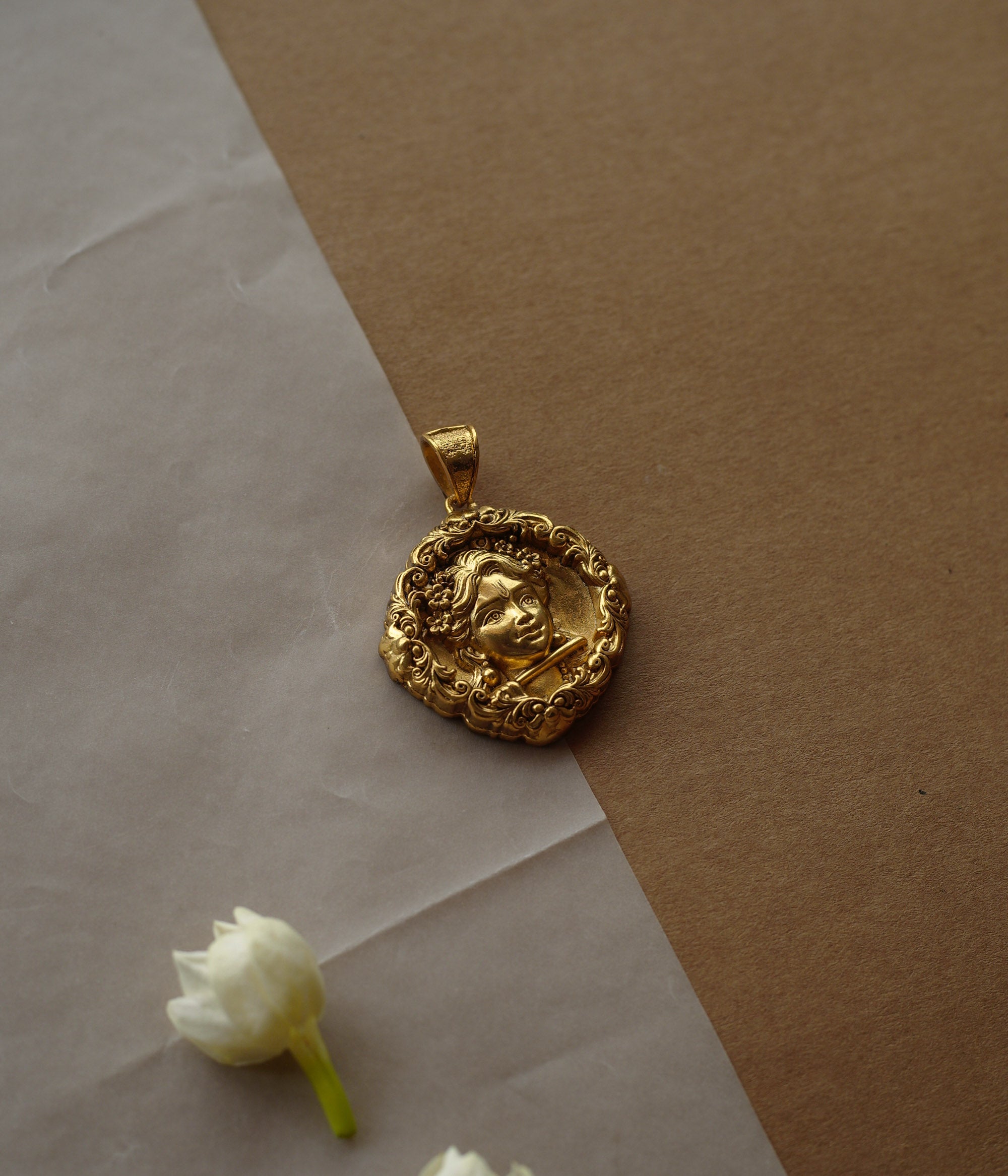 Round gold pendant with a central relief of a child's face. The face is surrounded by a detailed filigree border.