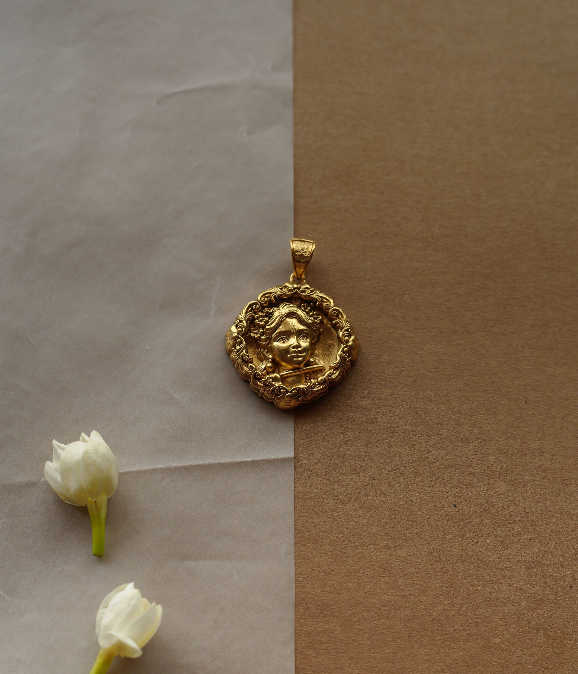 Round gold pendant with a central relief of a child's face. The face is surrounded by a detailed filigree border.
