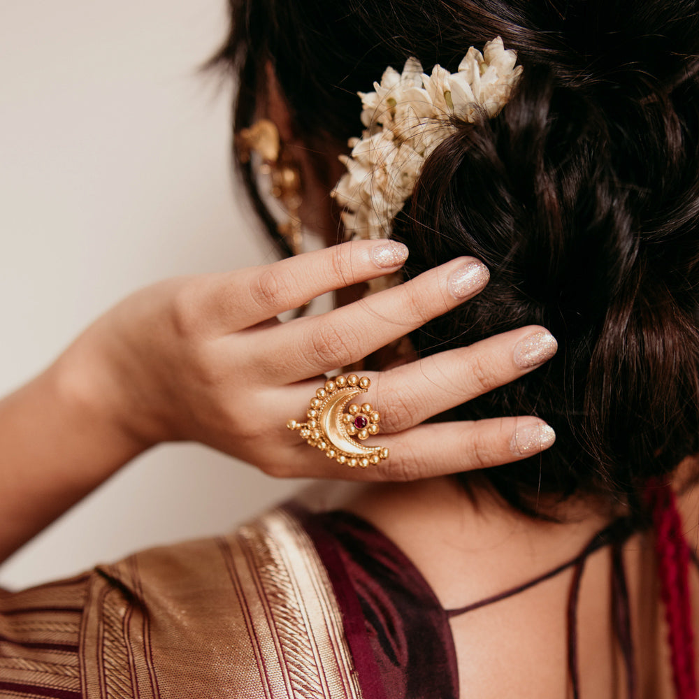 Temple-style crescent gold ring with red spinal stone, worn on hand with jasmine hair braid.
