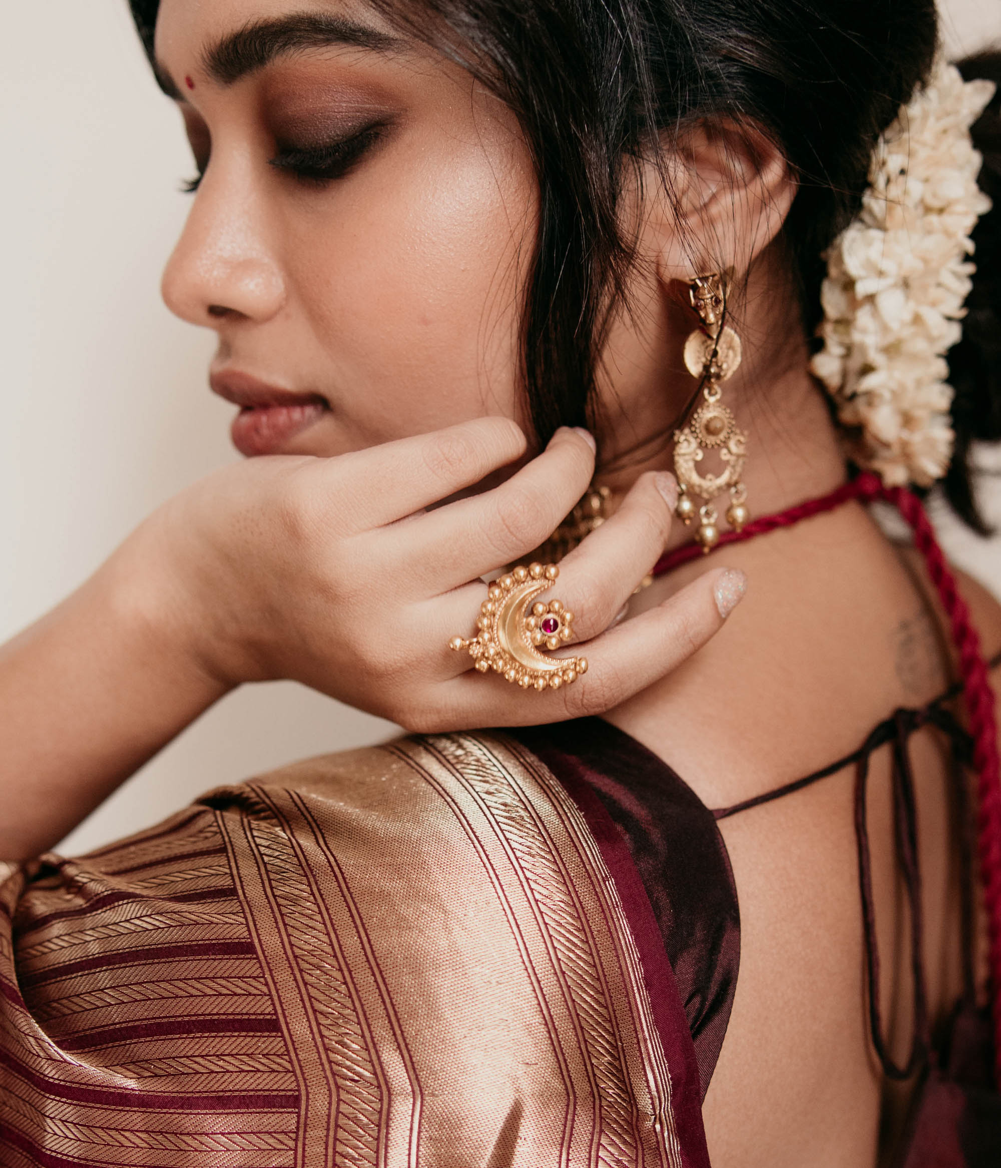 Temple-style crescent gold ring with red spinal stone, worn on hand with jasmine hair braid.