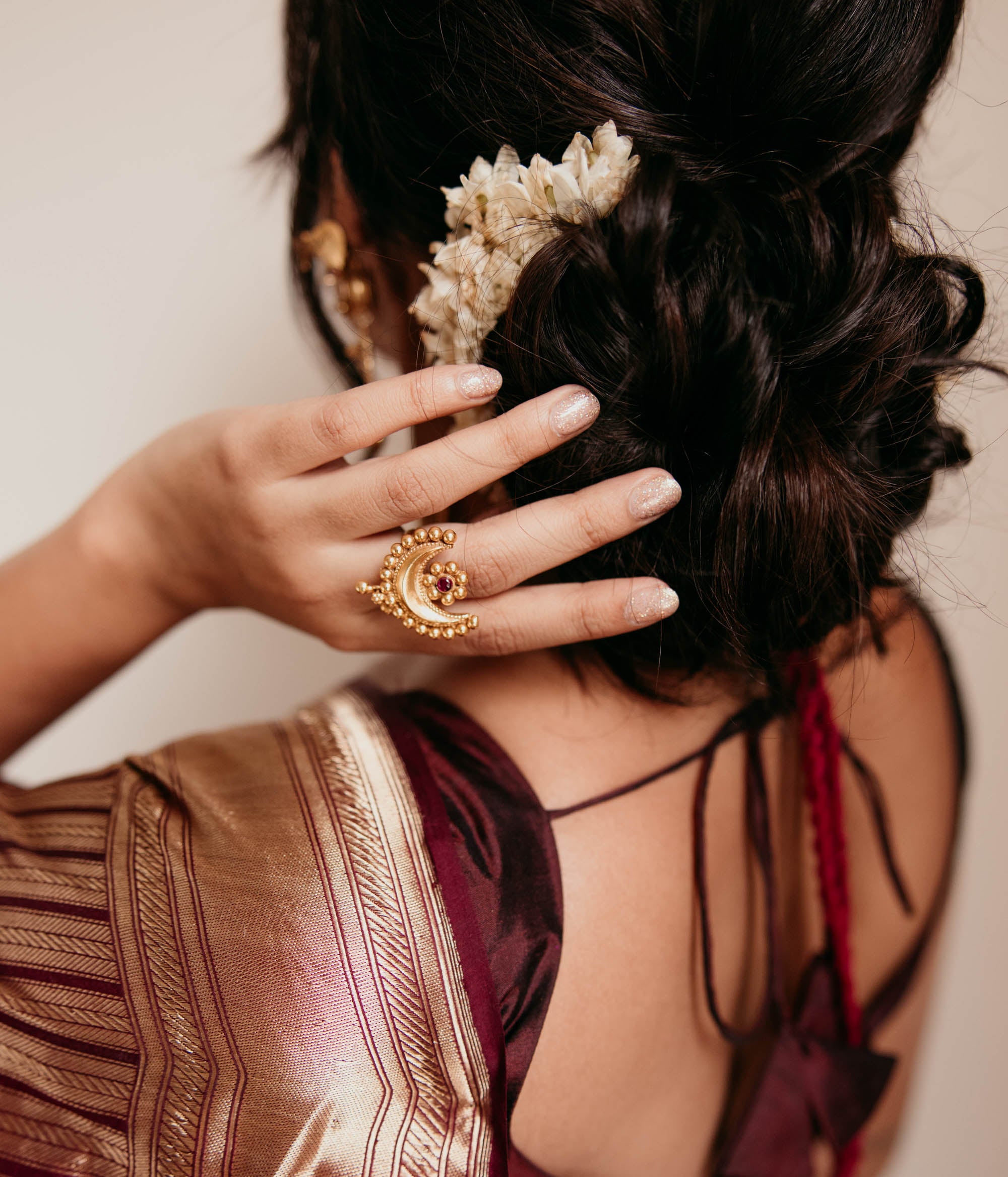 Temple-style crescent gold ring with red spinal stone, worn on hand with jasmine hair braid.