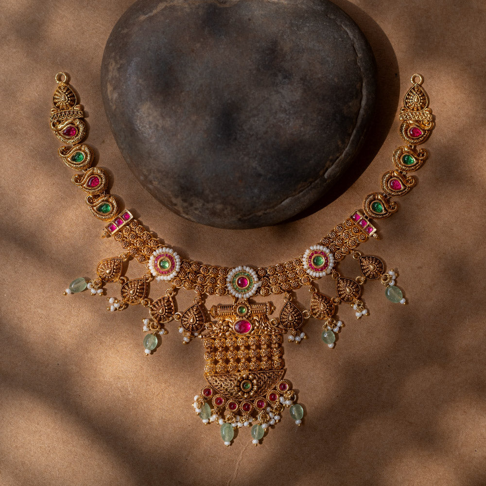 A 92.5 sterling silver Samhita Lakshmi Heritage Necklace with antique gold filigree, vibrant ruby and emerald accents, soft green drops, a divine Lakshmi pendant, and a pearl-laden fringe, echoing temple artistry for grand celebrations.