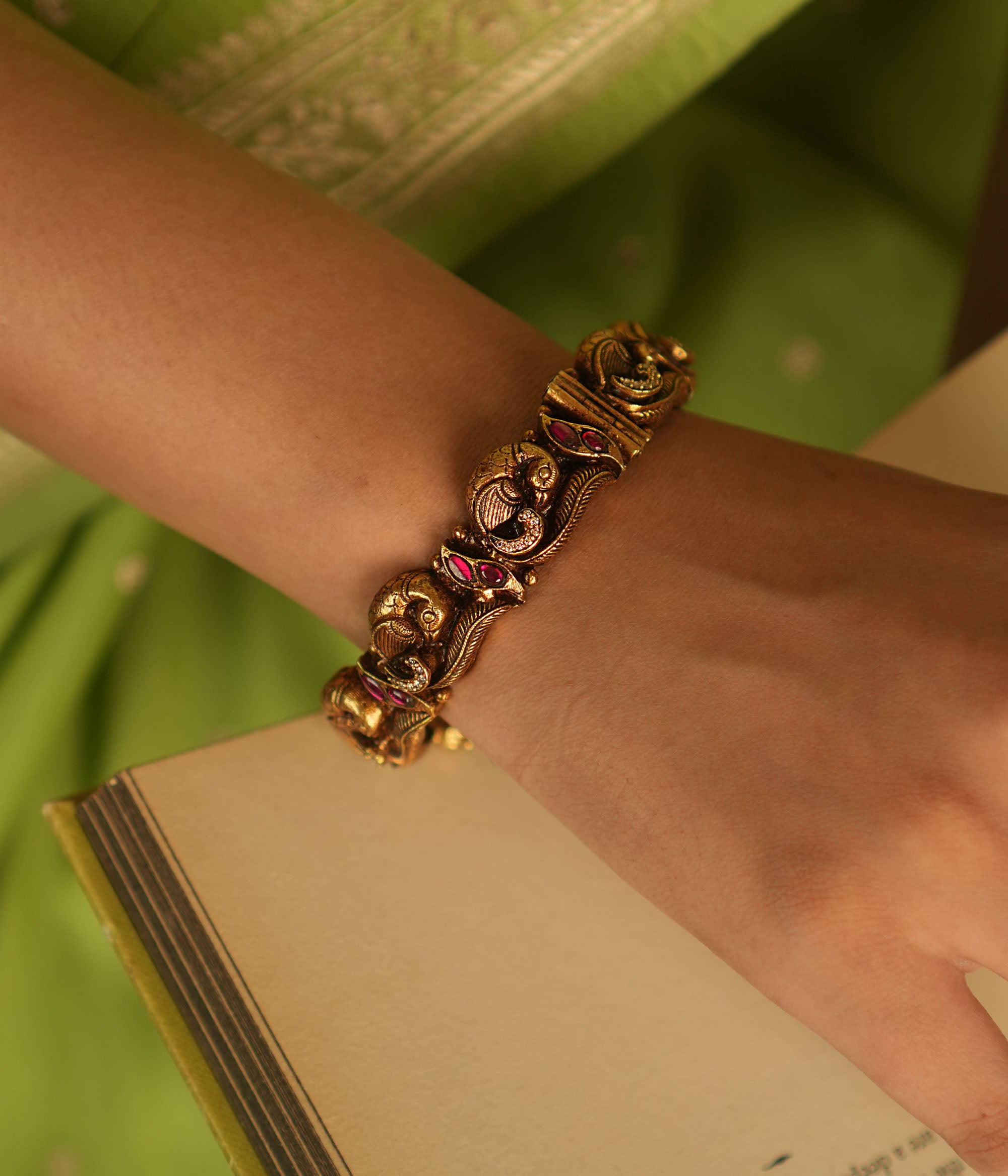 Antique gold-plated bangle with peacock motifs and pink kundan stones.