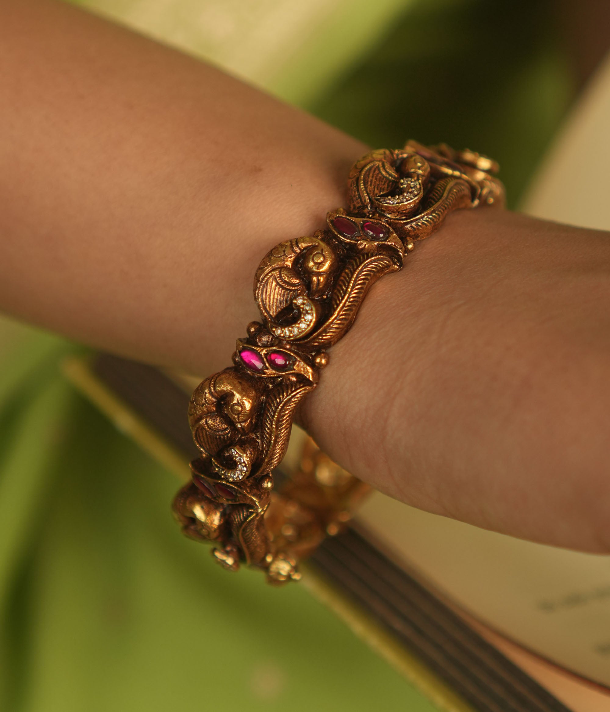 Antique gold-plated bangle with peacock motifs and pink kundan stones.