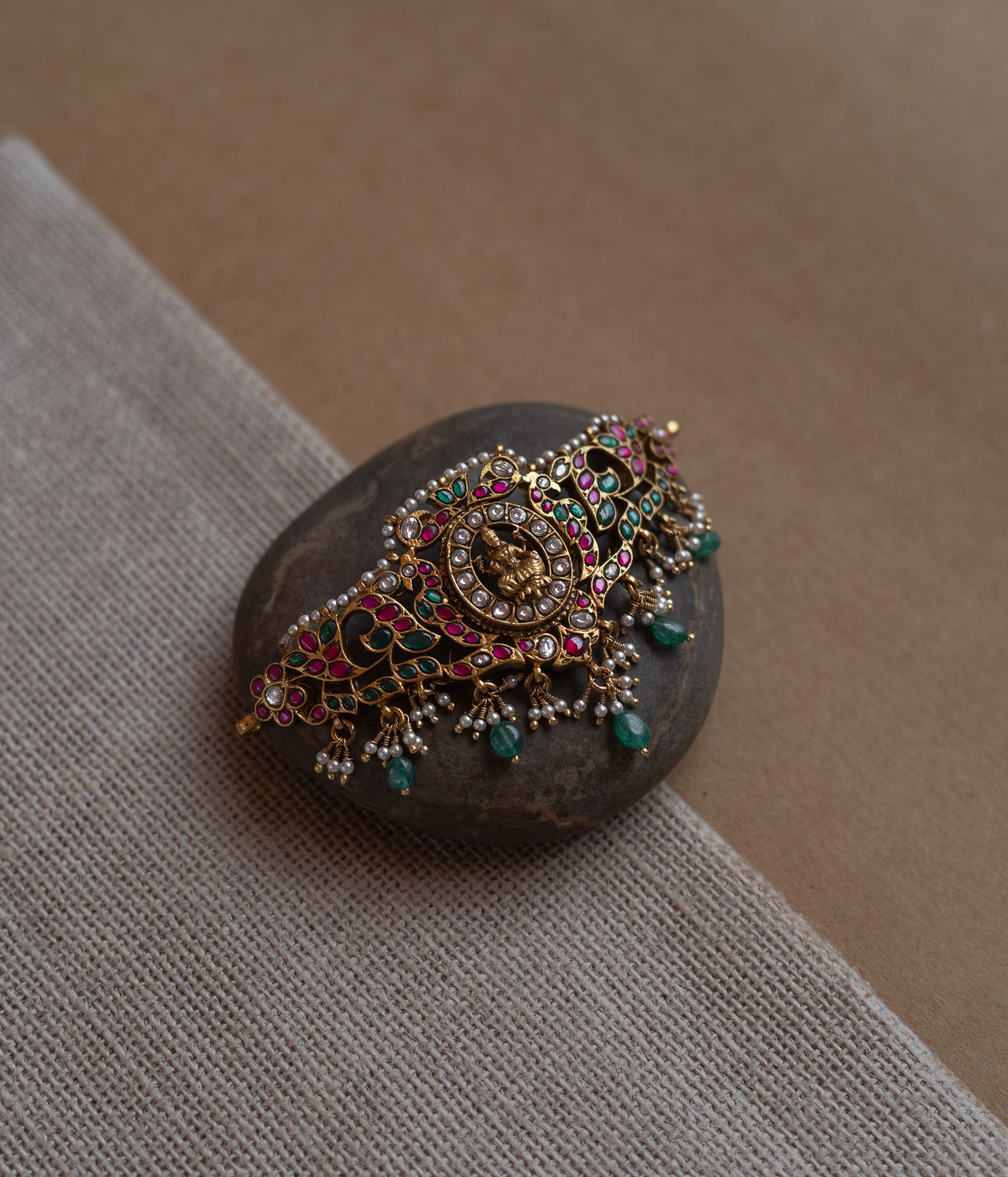 Temple-style choker with Lakshmi motif, kundan stones, pearls, and green beads on stone surface.