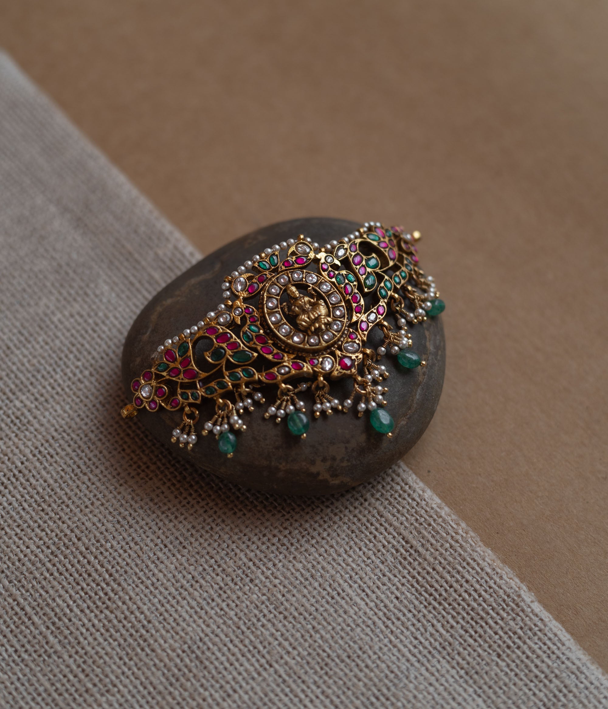 Temple-style choker with Lakshmi motif, kundan stones, pearls, and green beads on stone surface.