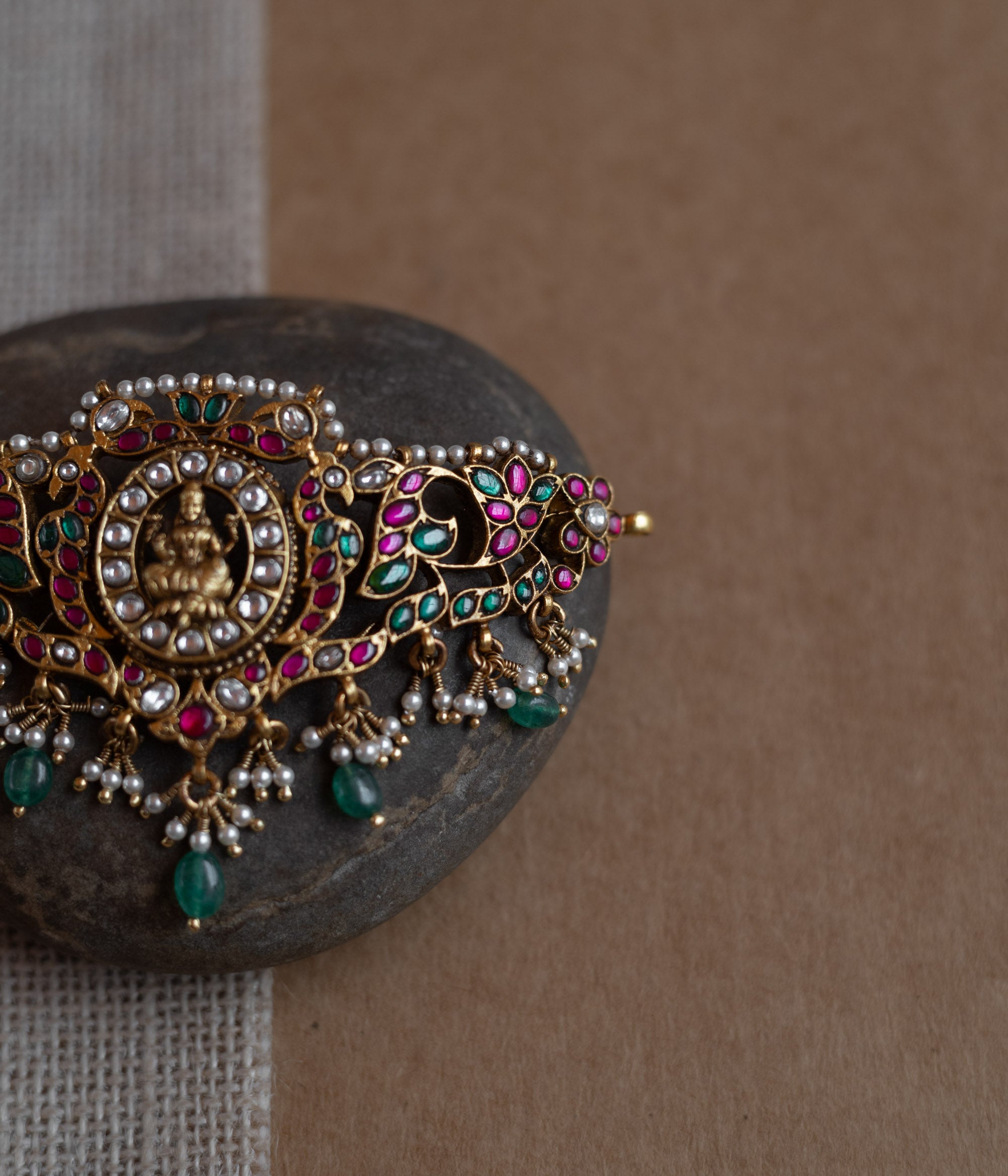 Temple-style choker with Lakshmi motif, kundan stones, pearls, and green beads on stone surface.