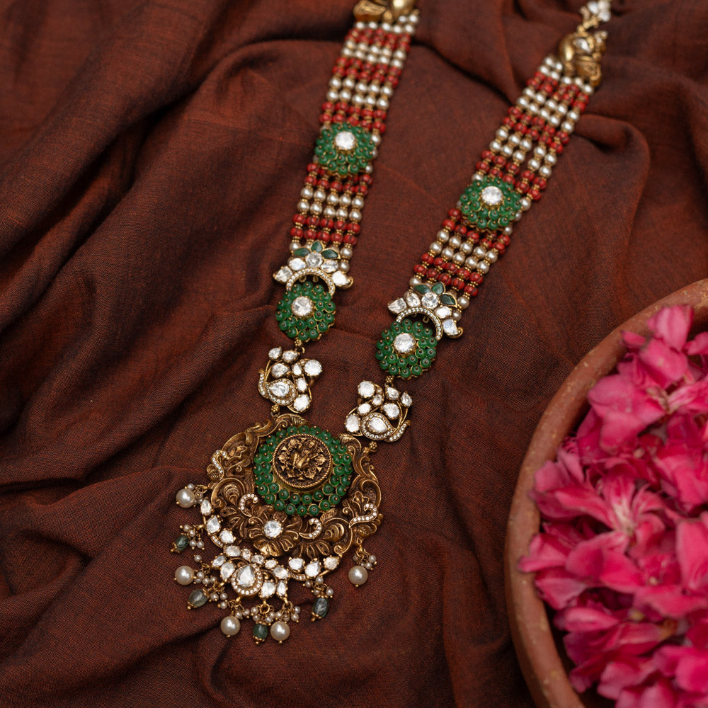 Antique gold-embossed 92.5 sterling silver Devi Lakshmi Necklace inspired by temple art, featuring vibrant green and white stones and cascading pearls from the divine central motif, embodying traditional elegance and spiritual grace.