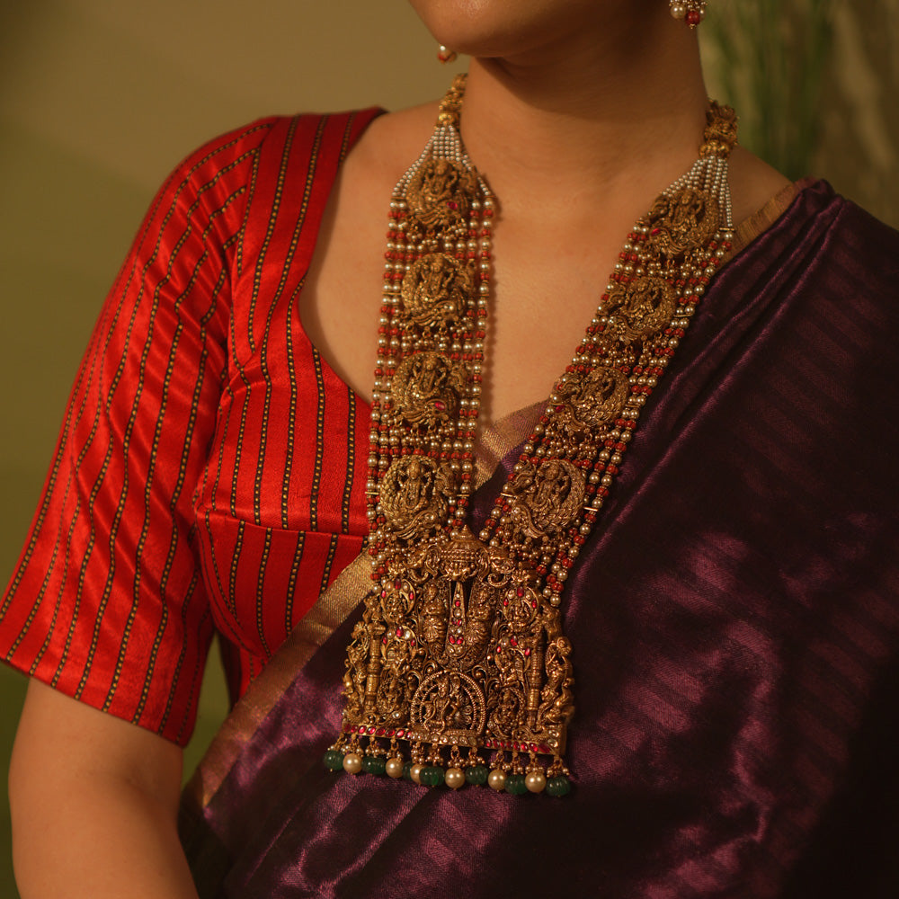 Temple necklace featuring goddess Lakshmi motifs, red and white Kundan stones, green beads, and pearls for traditional bridal wear.