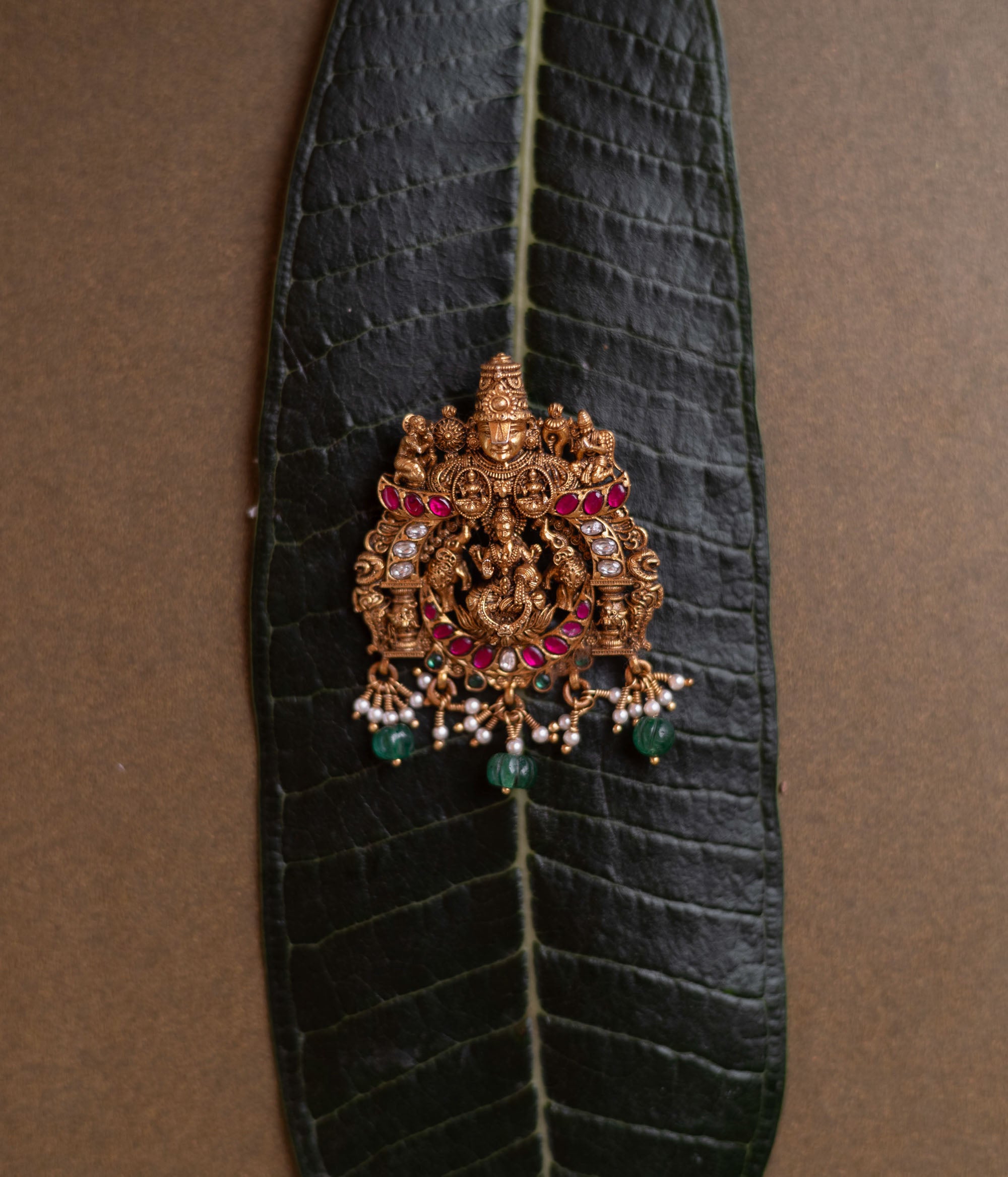 Temple pendant featuring Goddess Lakshmi with Garuda, detailed with red and white kundan and green beads.