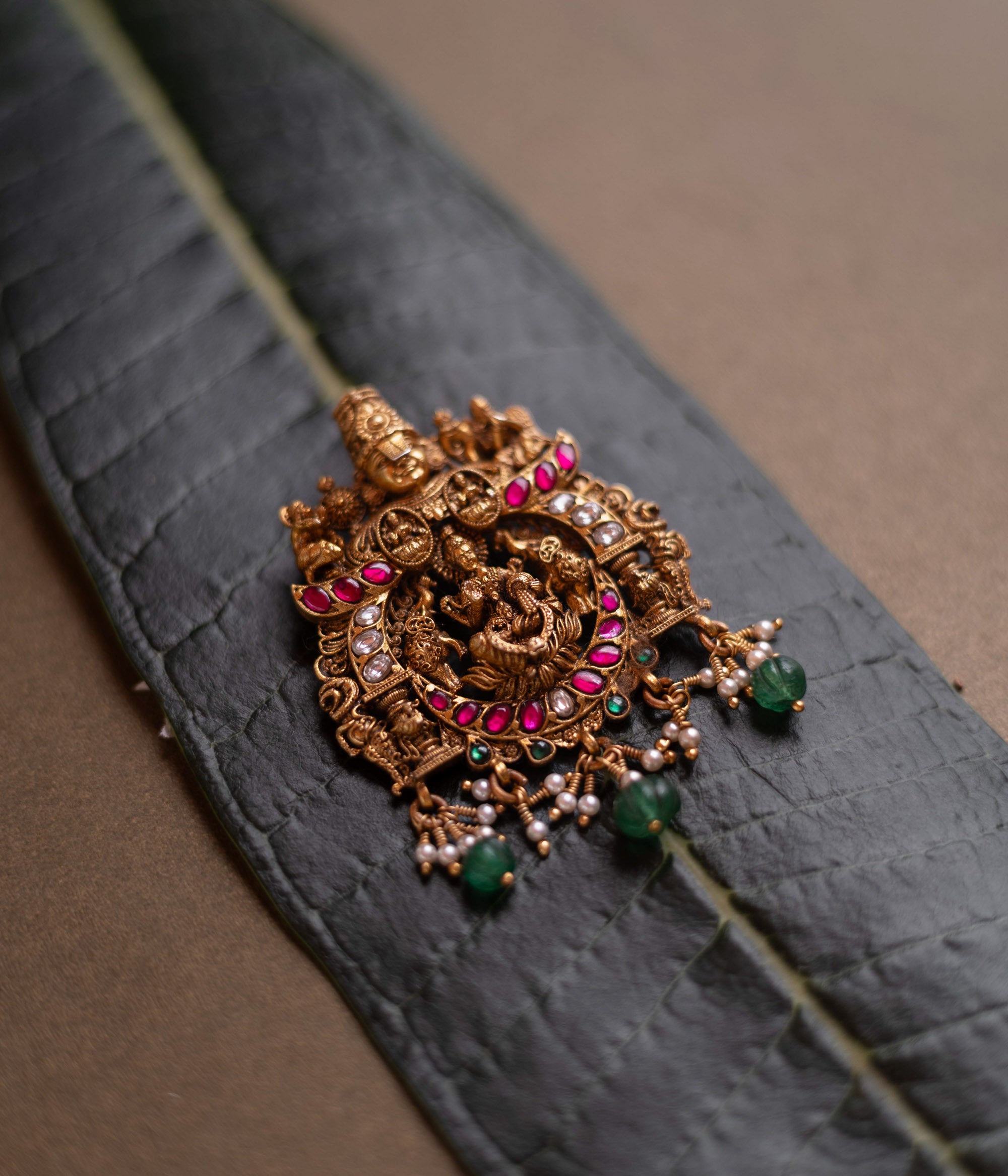 Temple pendant featuring Goddess Lakshmi with Garuda, detailed with red and white kundan and green beads.