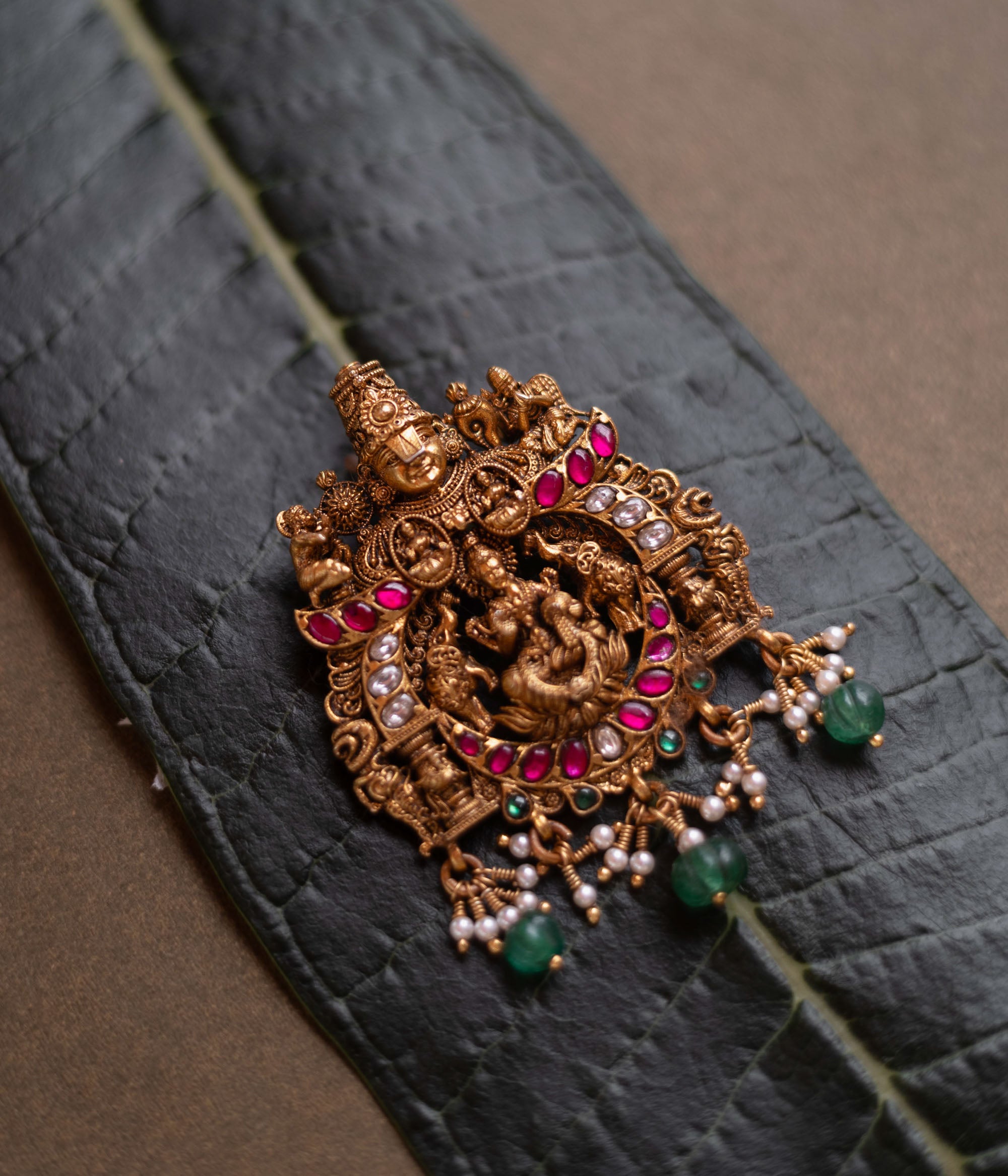 Temple pendant featuring Goddess Lakshmi with Garuda, detailed with red and white kundan and green beads.