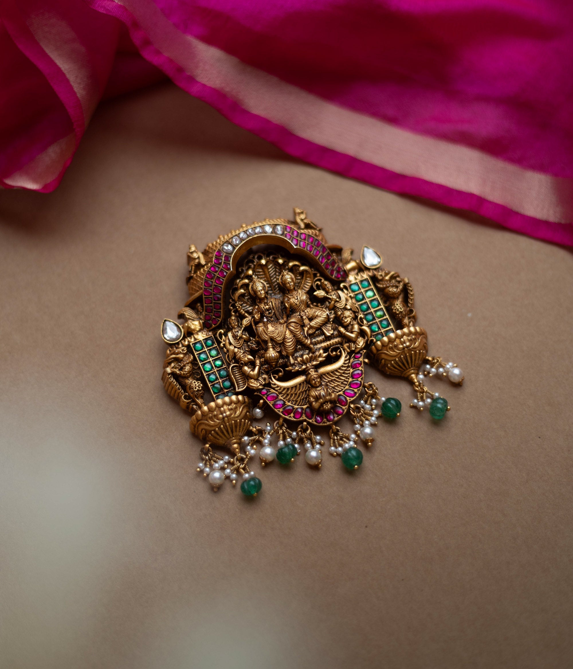 Antique gold temple pendant featuring deities, red, white, and green kundan, green beads, and pearls.