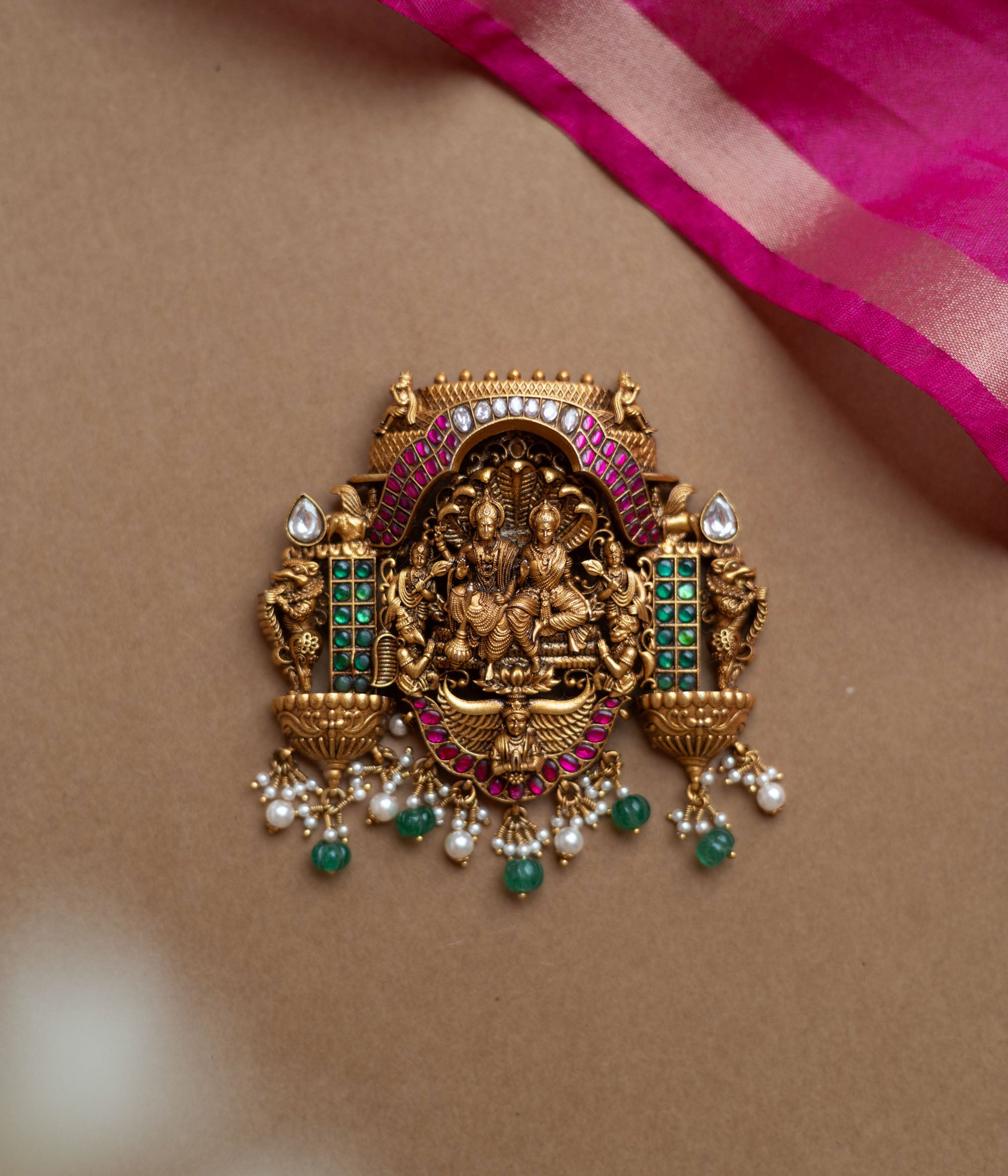 Antique gold temple pendant featuring deities, red, white, and green kundan, green beads, and pearls.