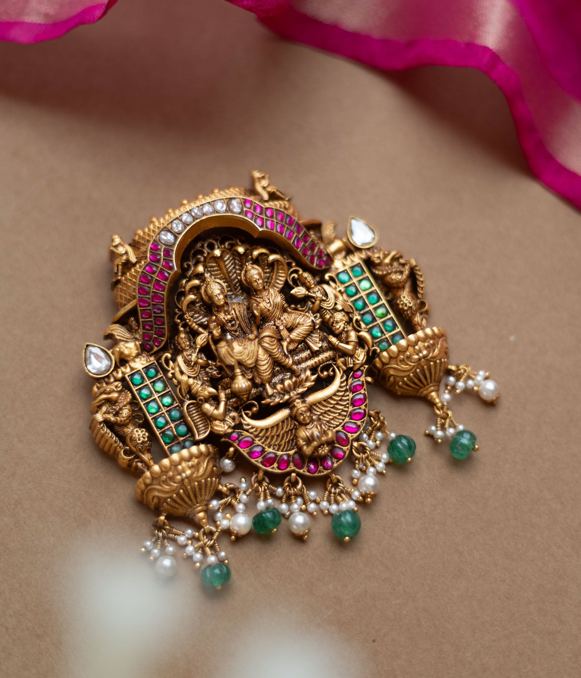 Antique gold temple pendant featuring deities, red, white, and green kundan, green beads, and pearls.