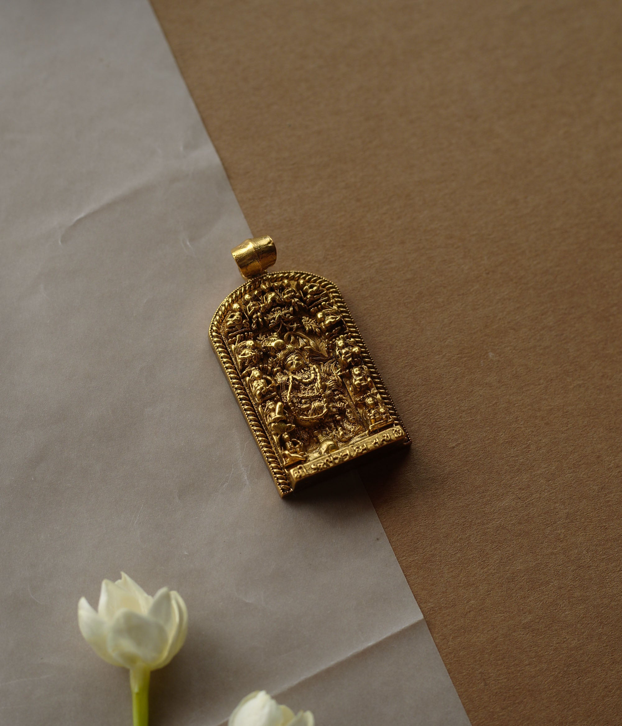 A gold pendant with a crescent-moon and floral design. It features a central red stone surrounded by clear stones and a halo of golden beads, resting on a stone.