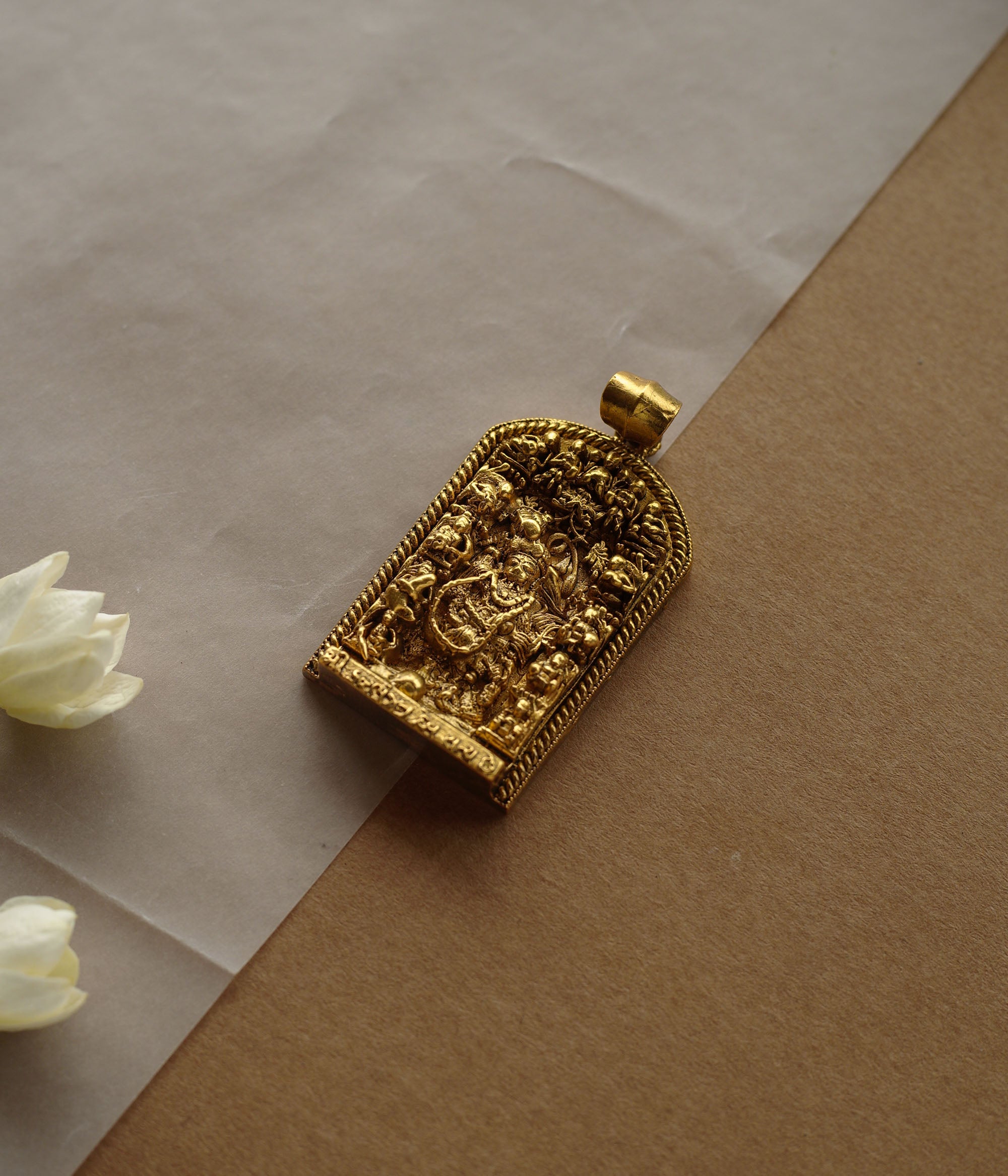 A gold pendant with a crescent-moon and floral design. It features a central red stone surrounded by clear stones and a halo of golden beads, resting on a stone.