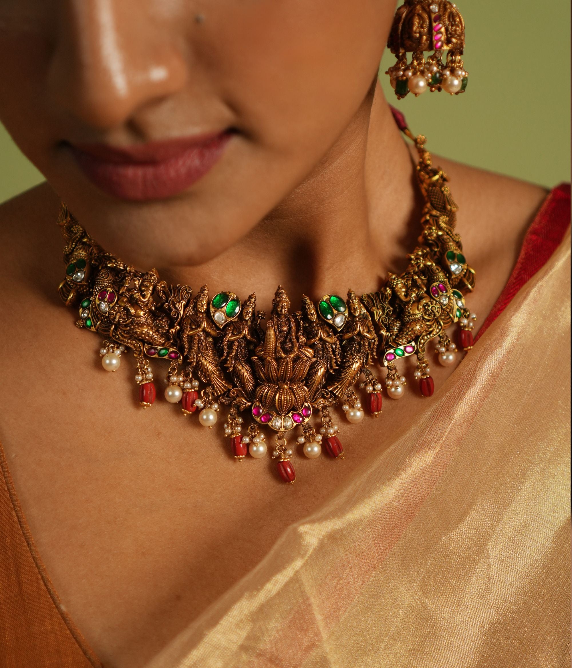 Gold-plated silver temple jewellery necklace featuring detailed carvings of Goddess Lakshmi and Lord Ganesh, adorned with red Kundan stones, white Kundan stones, white pearls, and red beads, exuding a regal and divine charm.