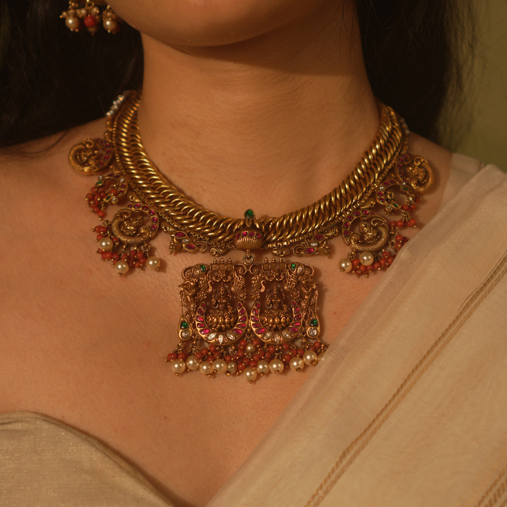 Gold temple necklace with pink kundan peacock pendants, carved deity, pearls, and coral.