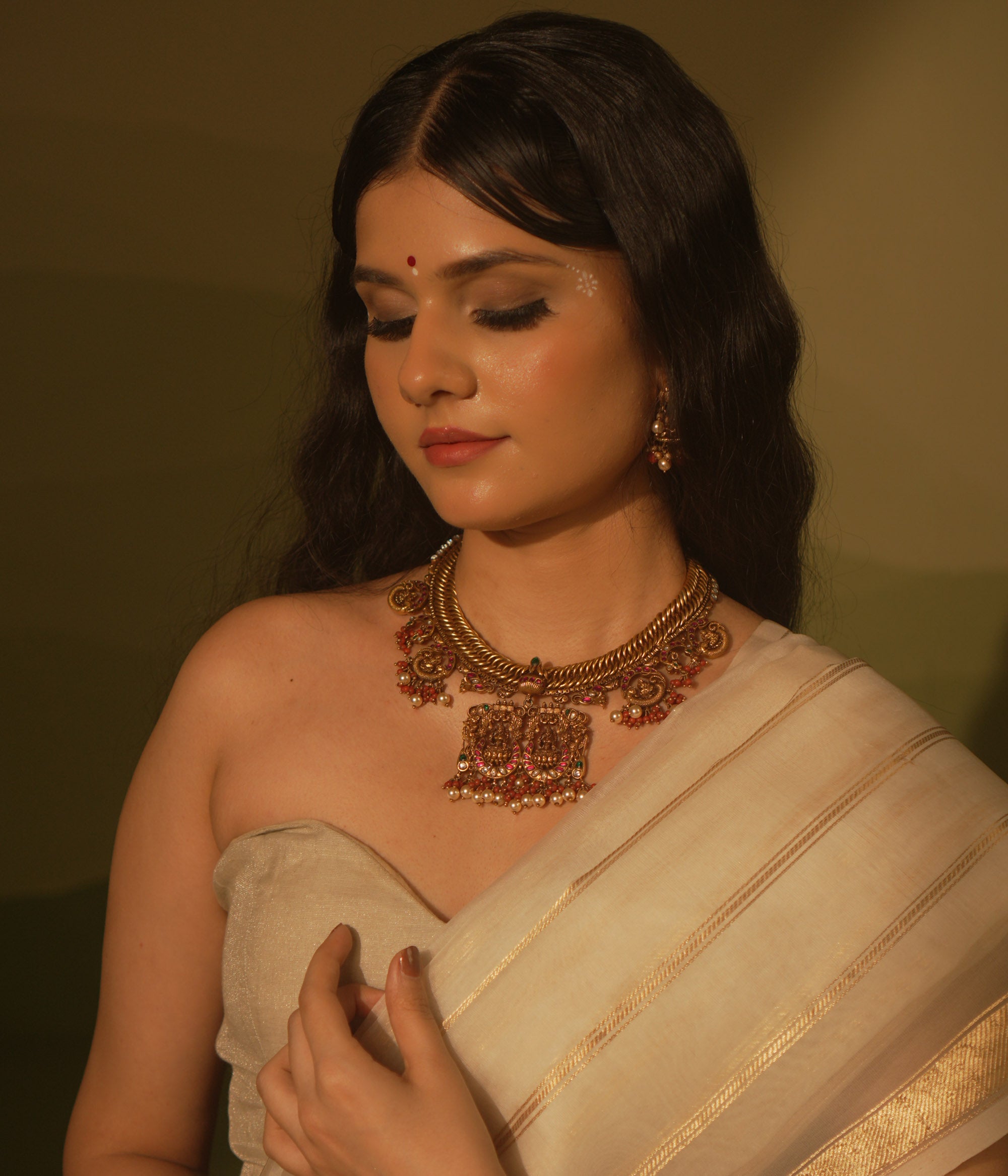 Gold temple necklace with pink kundan peacock pendants, carved deity, pearls, and coral.