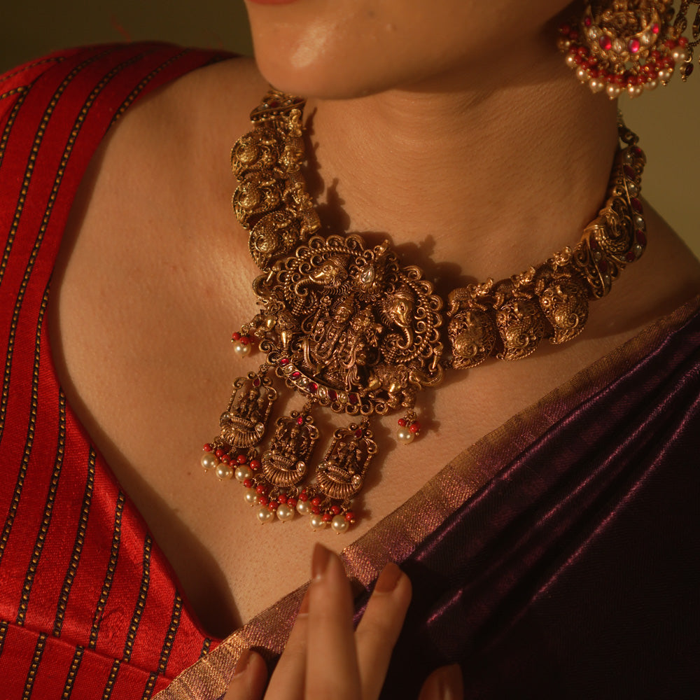 Simhika temple necklace with goddess motifs, lion guardians, red Kundan stones, and pearl detailing.