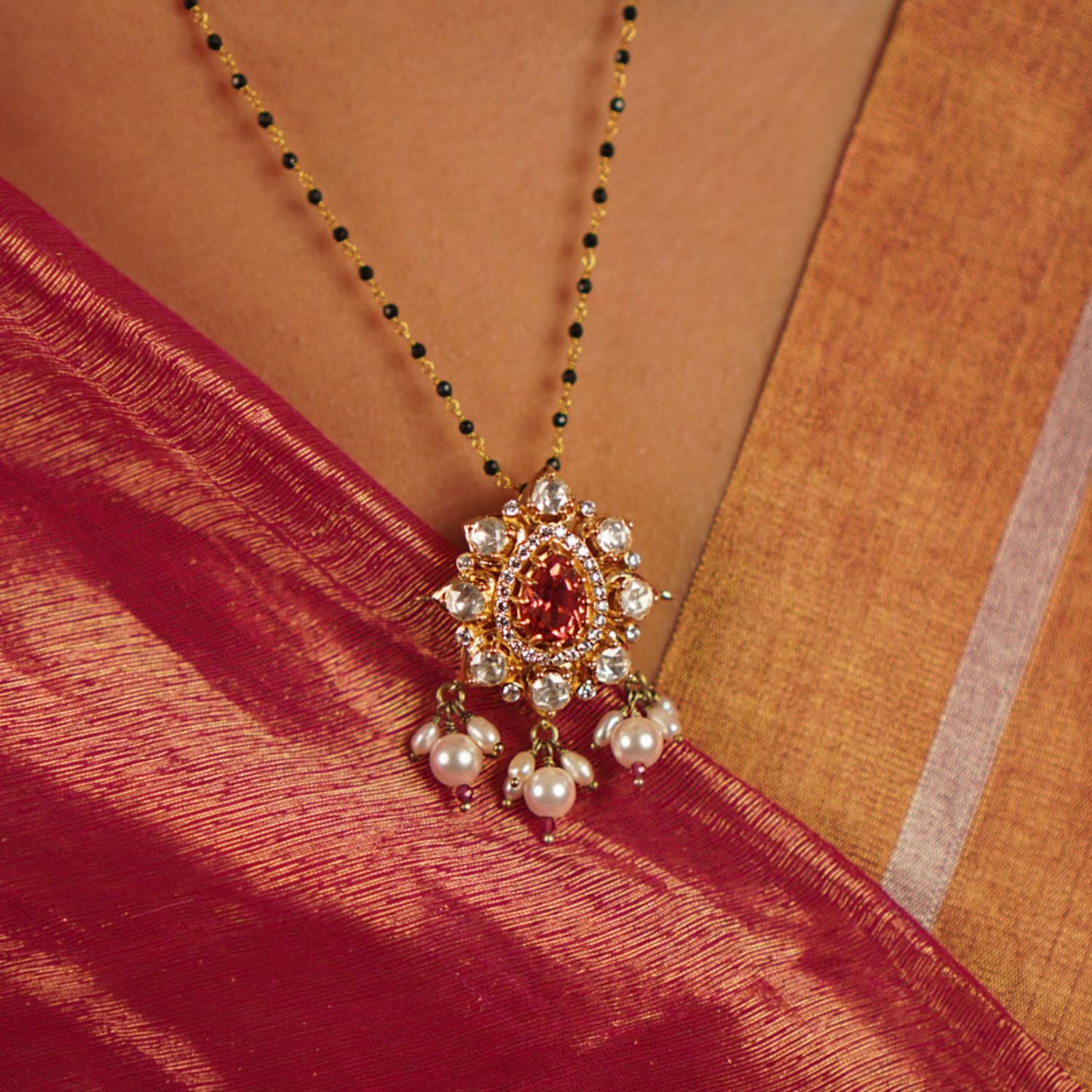 This mangalsutra features a vibrant ruby at its center, surrounded by moissanite polki in an elegant floral design, gracefully accented with freshwater pearl drops.