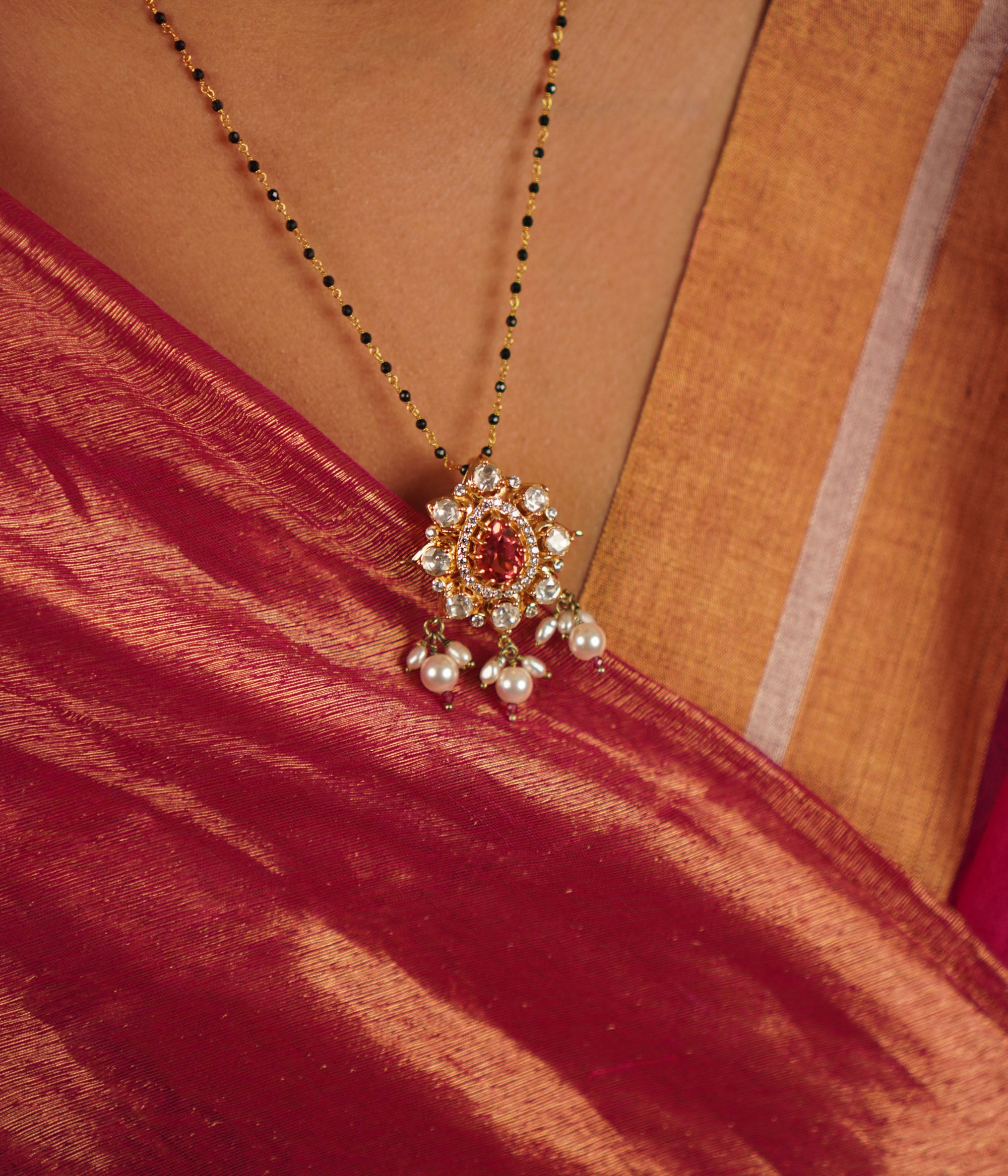 This mangalsutra features a vibrant ruby at its center, surrounded by moissanite polki in an elegant floral design, gracefully accented with freshwater pearl drops.
