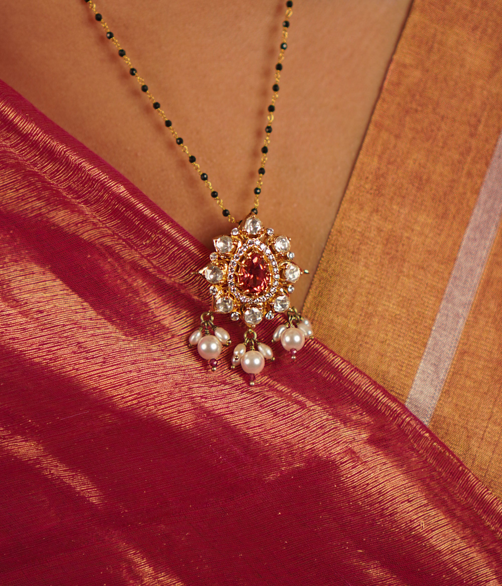 This mangalsutra features a vibrant ruby at its center, surrounded by moissanite polki in an elegant floral design, gracefully accented with freshwater pearl drops.