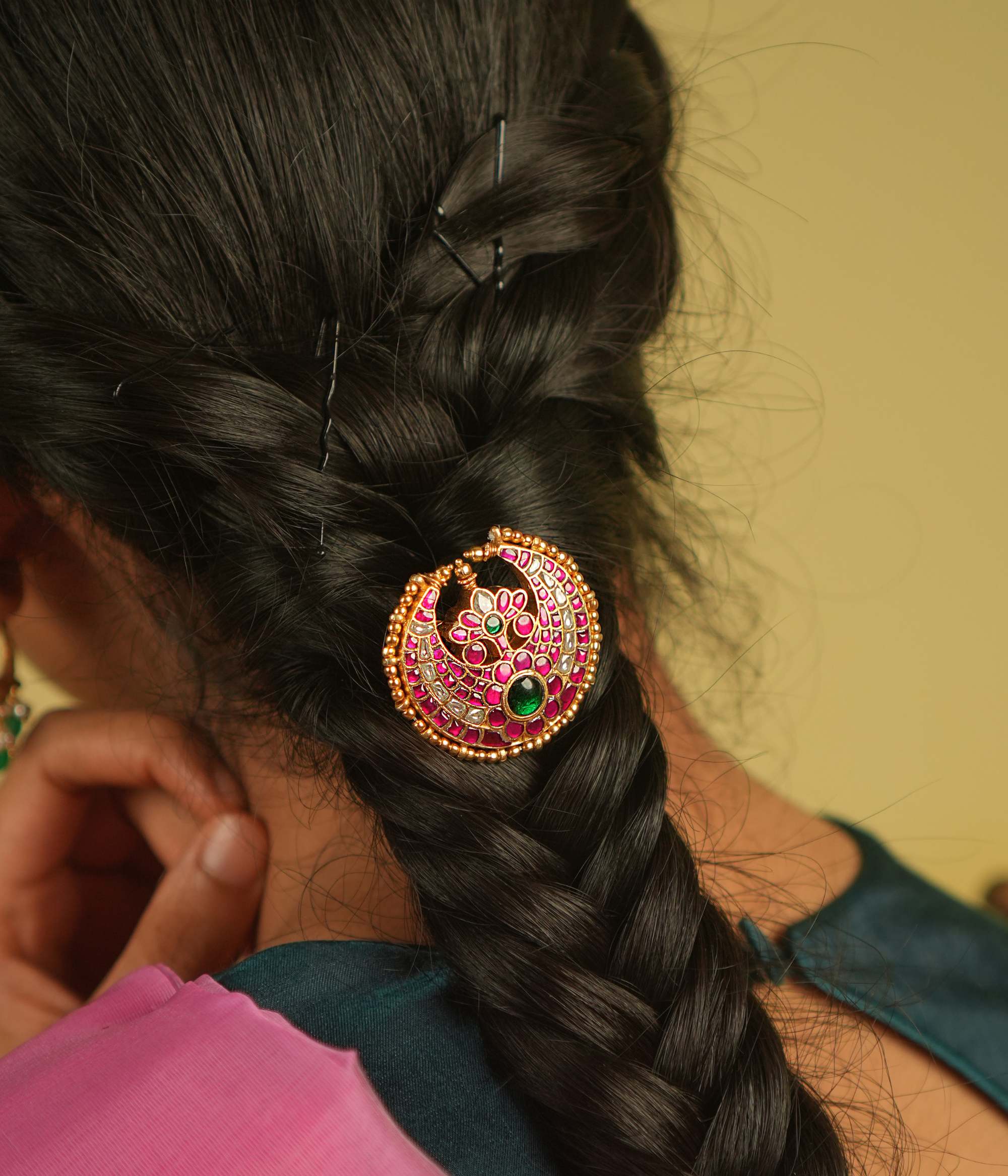 A crescent moon hairpin, embellished with soft pink Kundan and a captivating emerald at its heart, exudes celestial charm and timeless elegance.