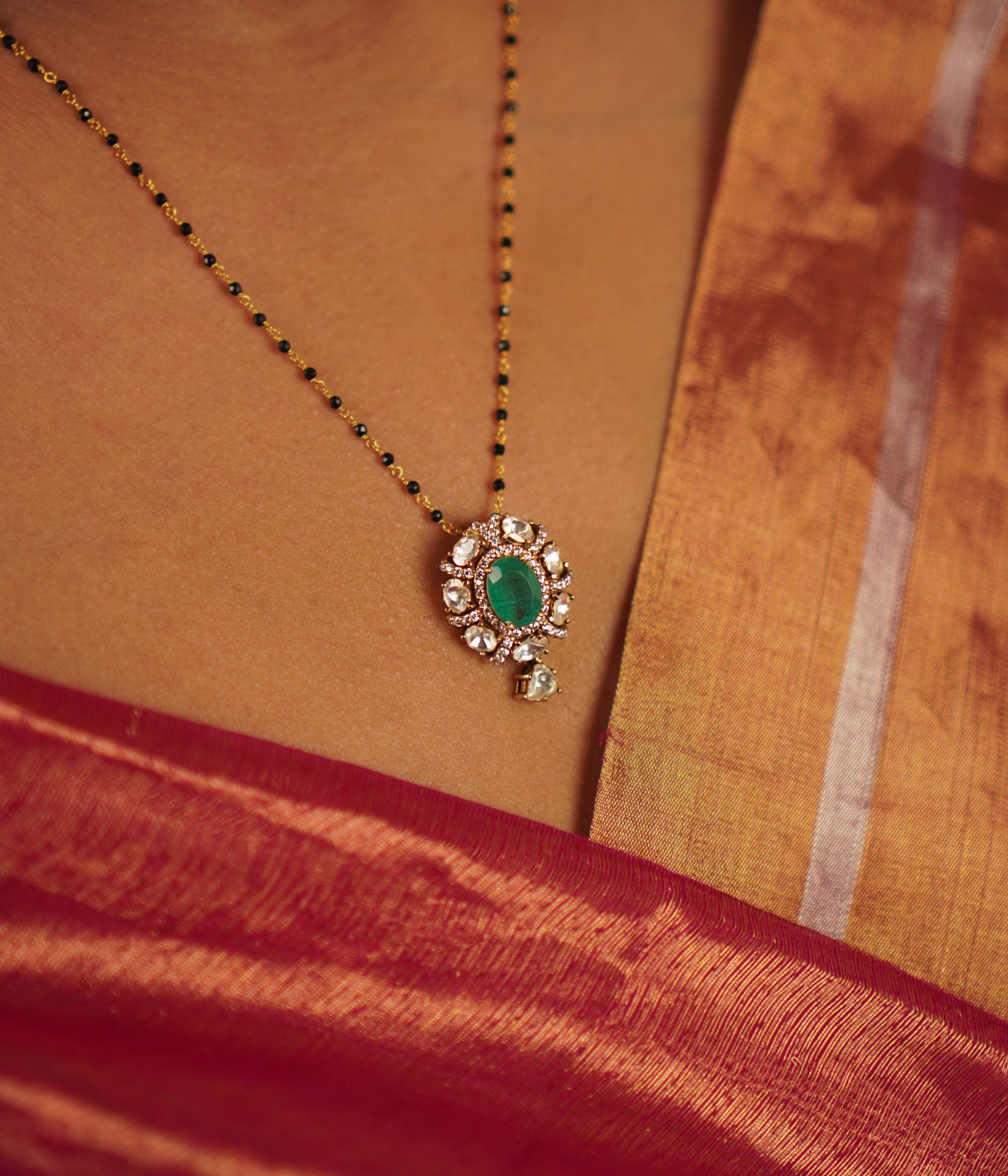 The Devya Mangalsutra, designed in gold-plated silver, showcases a radiant polki arrangement with a striking emerald centerpiece. A harmonious fusion of heritage and contemporary elegance.