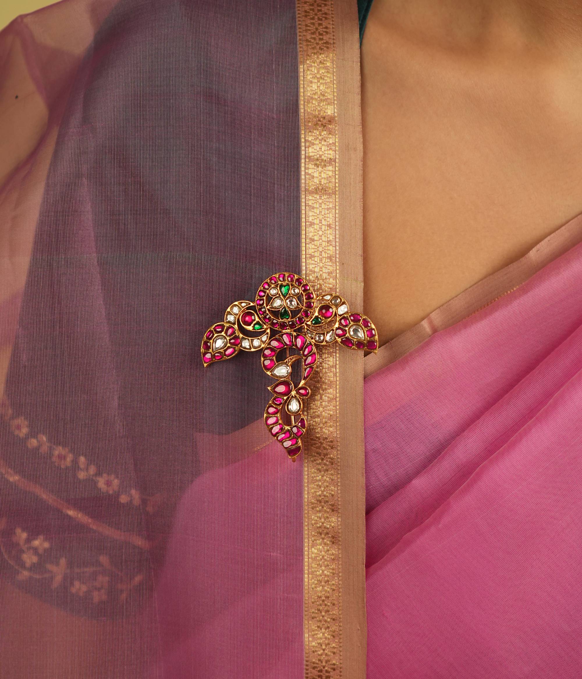 A meticulously designed floral saree brooch, embellished with radiant red, green, and white Kundan, exudes timeless regal charm.