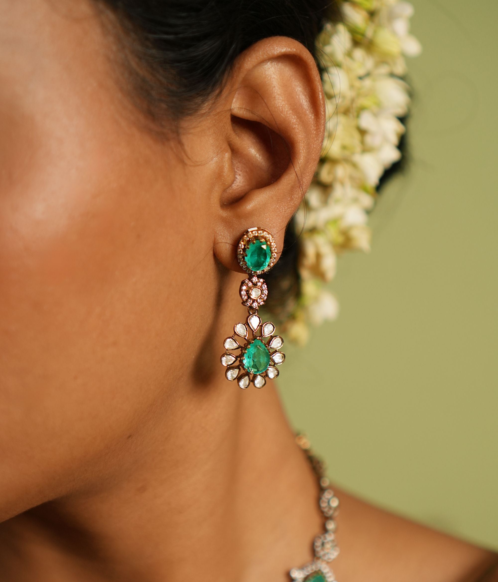 Elegant gold-plated silver drop earrings adorned with moissanite Polki stones, CZ stones, and vibrant green gemstones, and has a flower design offering a timeless and sophisticated design for any occasion.