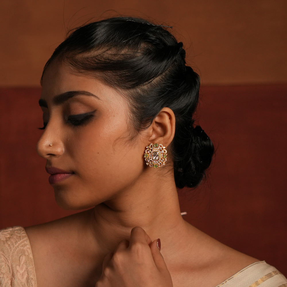 A beautifully crafted gold-plated silver stud earring featuring a dazzling Polki stone at the center, elegantly surrounded by a layer of shimmering CZ stones and vibrant green cut stones. This exquisite design adds a touch of sophistication, making it a perfect accessory for both traditional and contemporary looks.