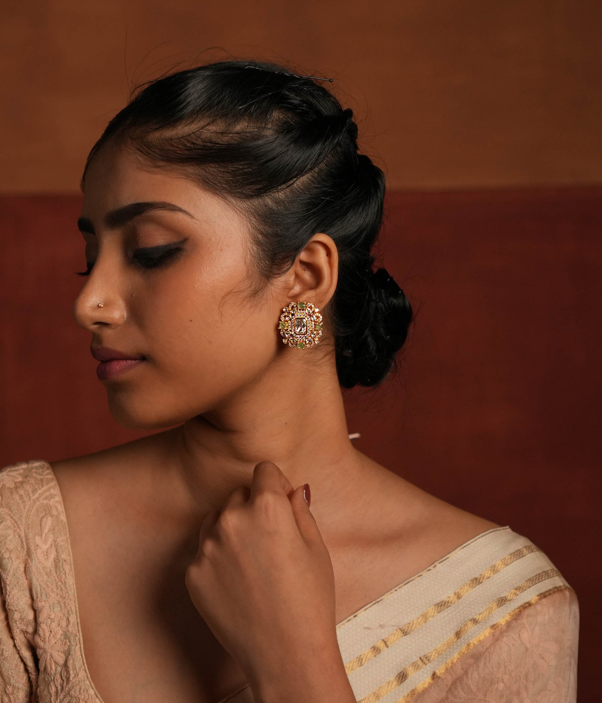 A beautifully crafted gold-plated silver stud earring featuring a dazzling Polki stone at the center, elegantly surrounded by a layer of shimmering CZ stones and vibrant green cut stones. This exquisite design adds a touch of sophistication, making it a perfect accessory for both traditional and contemporary looks.